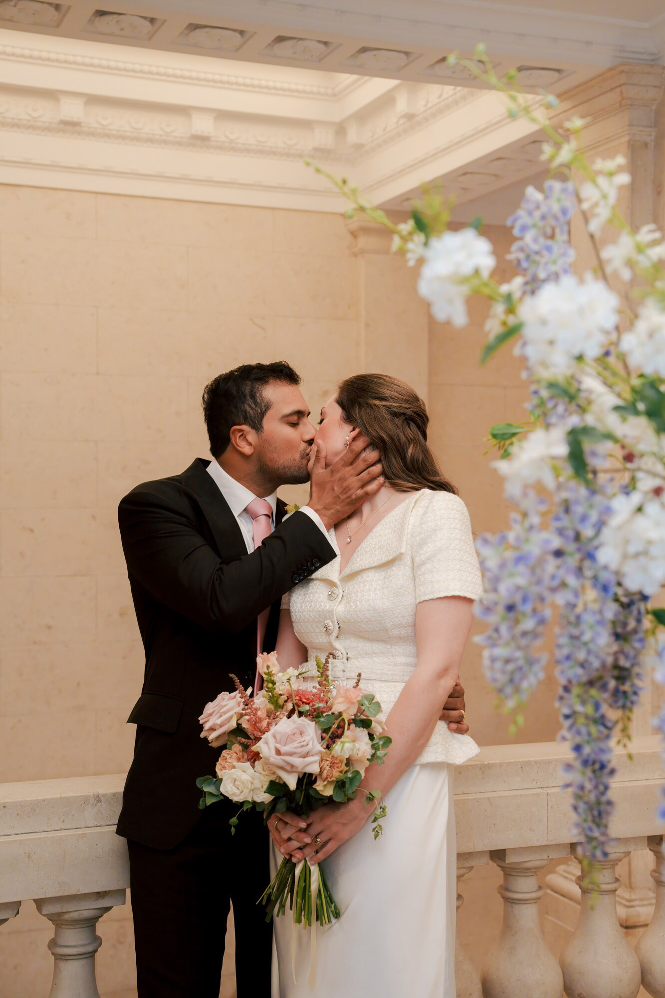 Bride and groom kissing beside a wisteria flower arrangement on the town hall staircase
