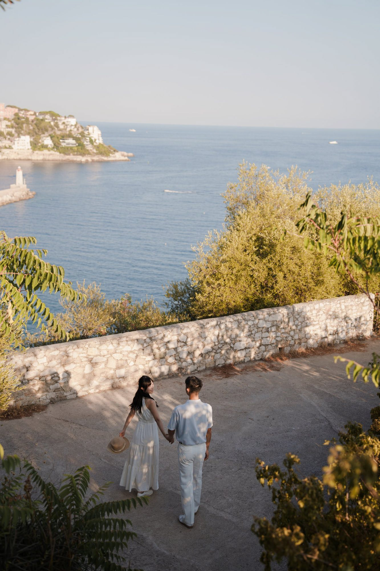 Walking hand in hand on Castle Hill in Nice at sunset, the harbour lighthouse below