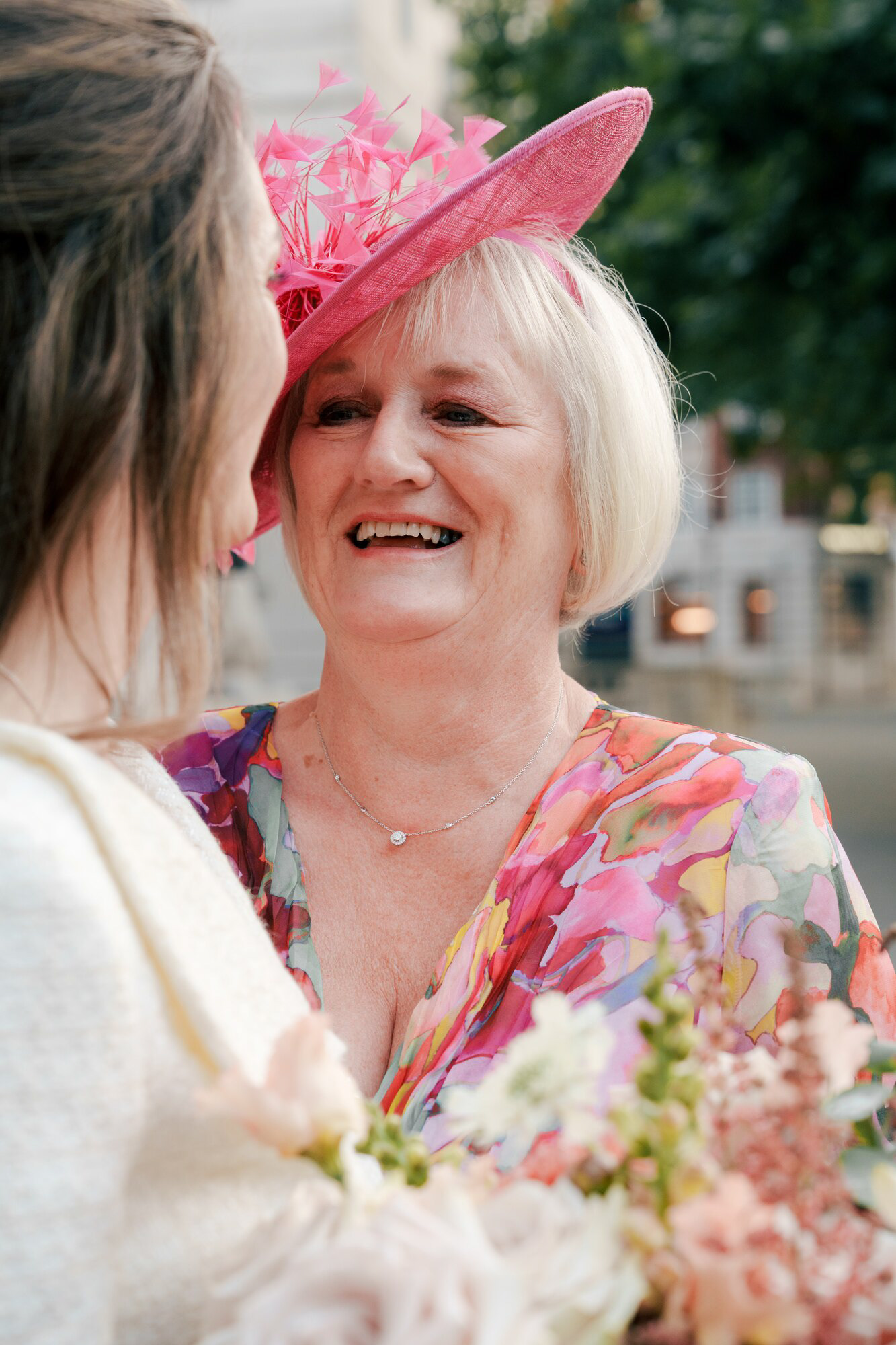 Guest in a pink fascinator beaming at the bride outside Marylebone Town Hall