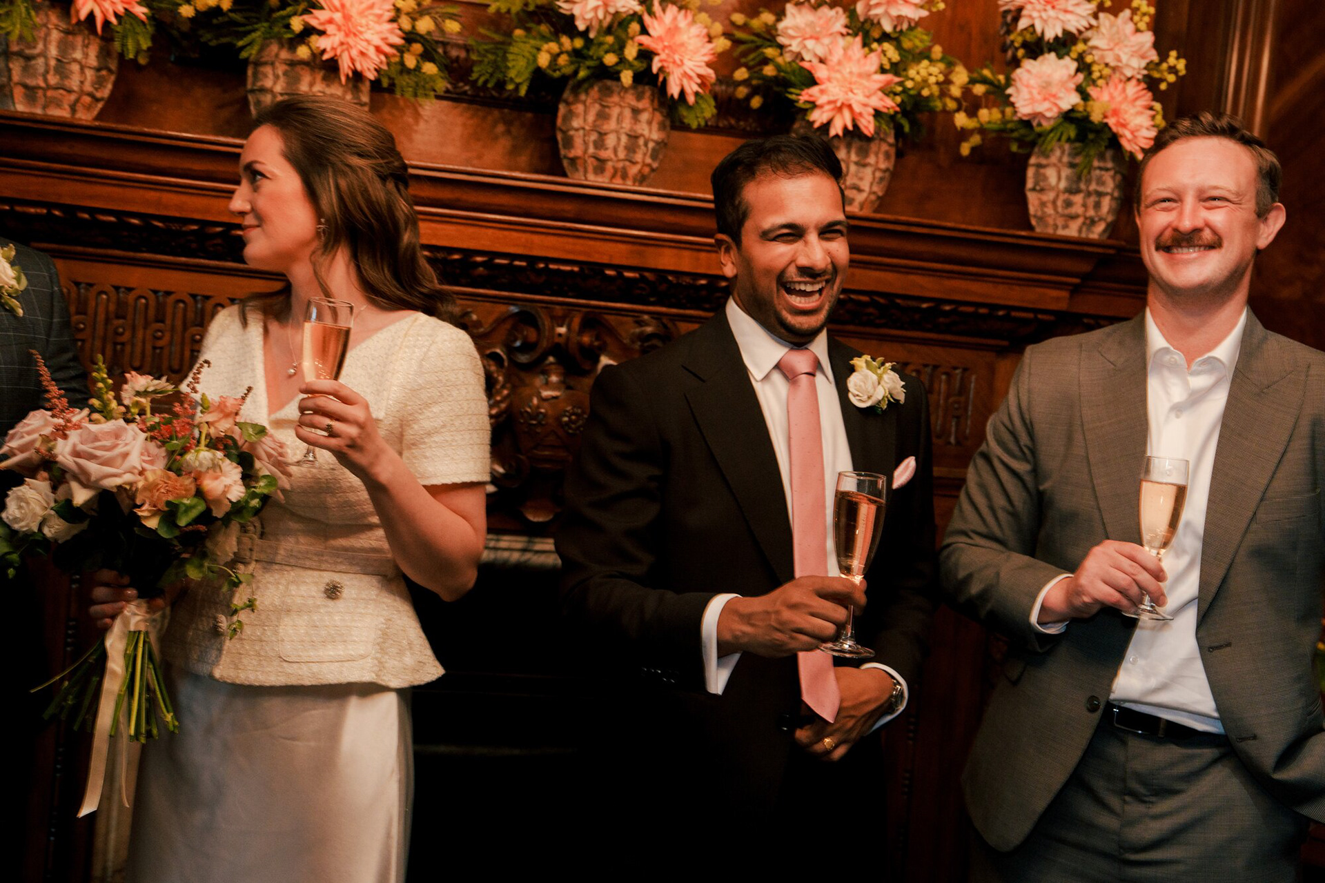 Bride, groom and a friend laughing over champagne after the ceremony