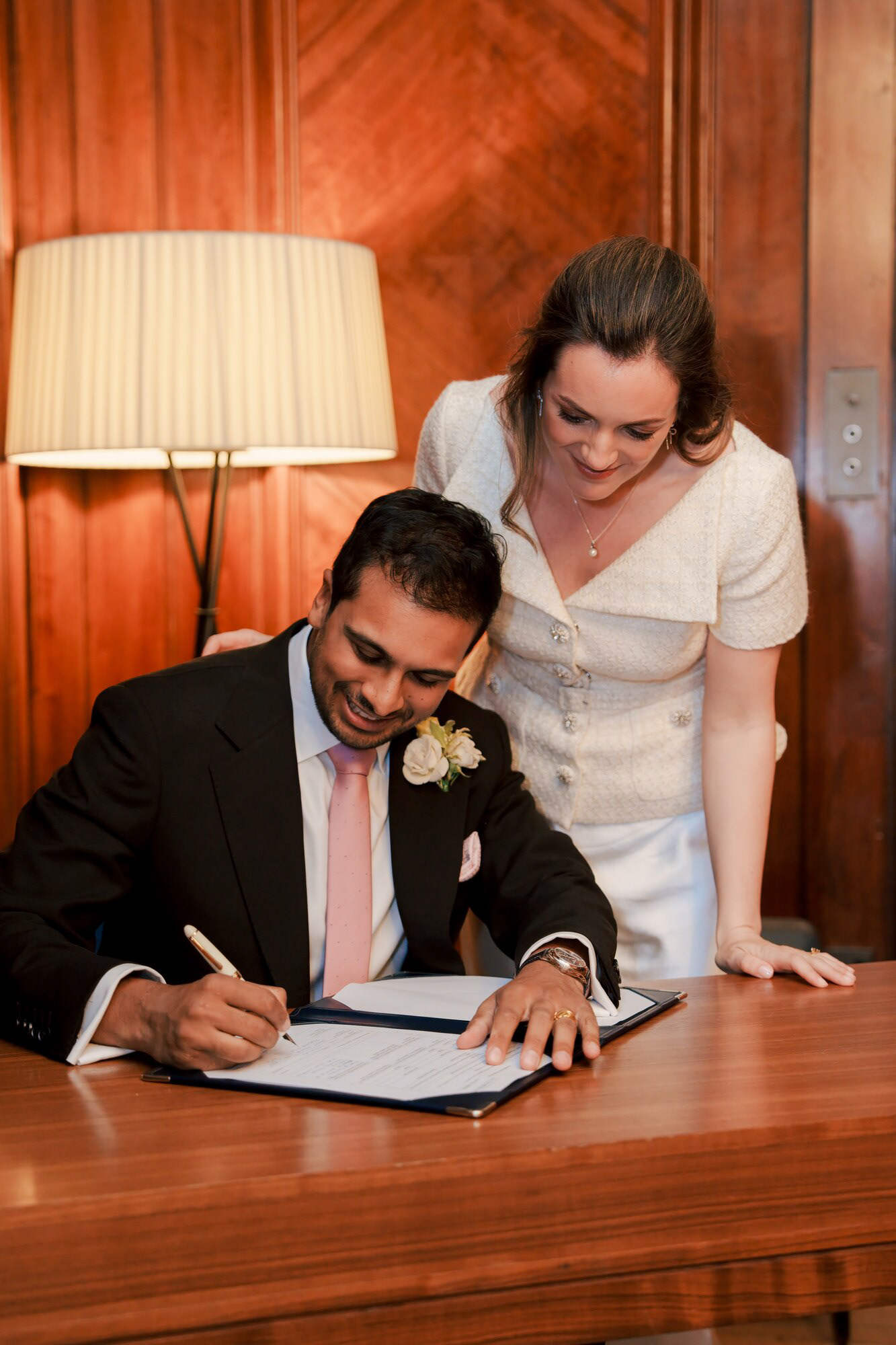 Groom signing the wedding register as the bride watches at Marylebone Town Hall