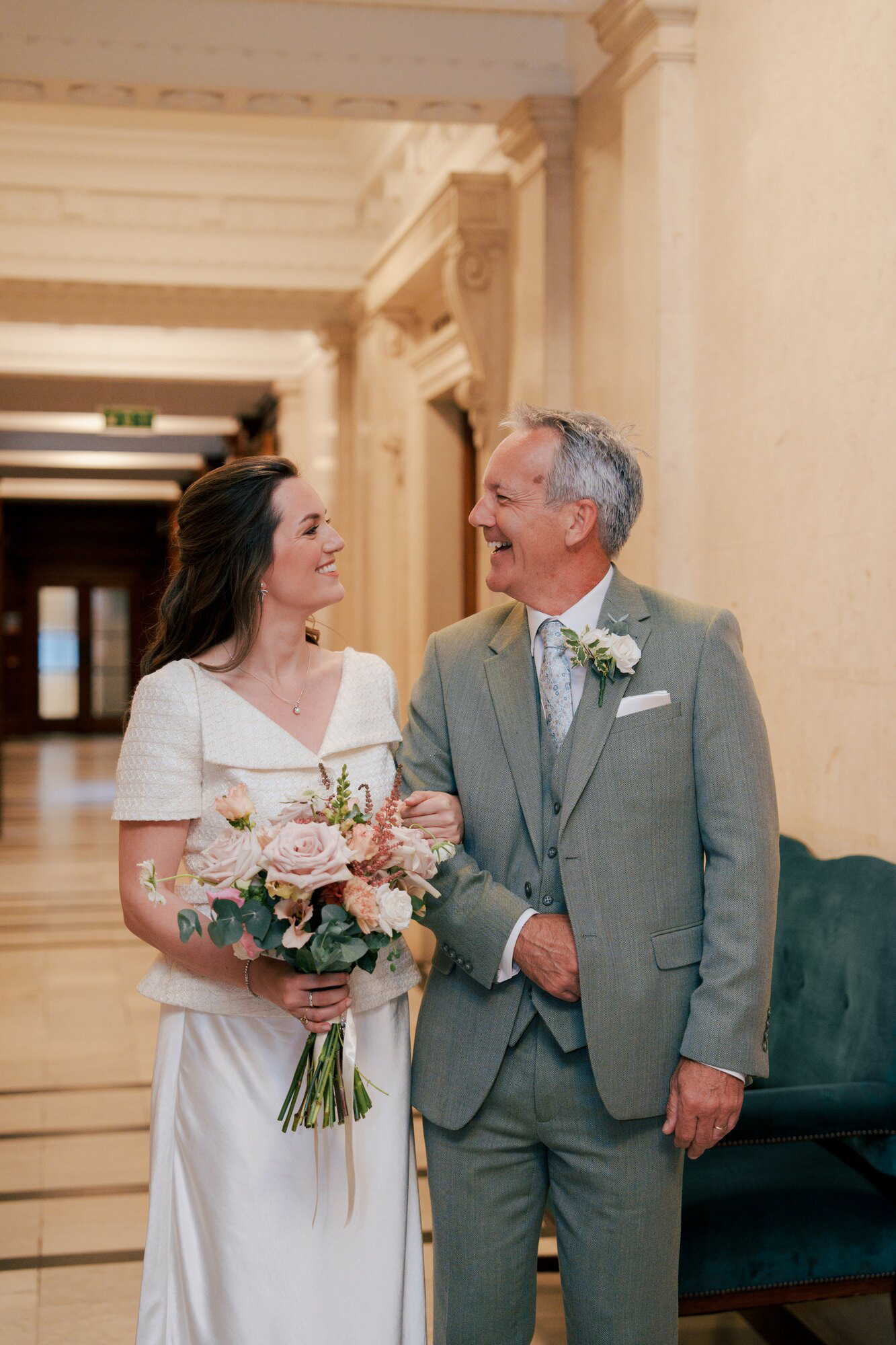 Bride walking arm in arm with a family member through the marble corridor of Old Marylebone Town Hall