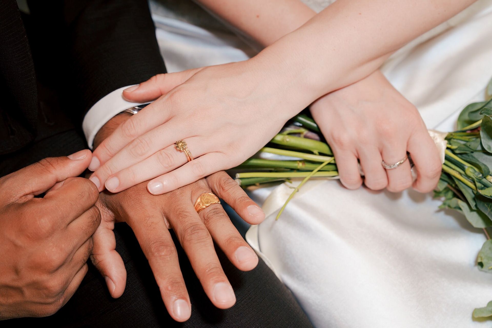 Close-up of the couple's hands and wedding rings over the bridal bouquet
