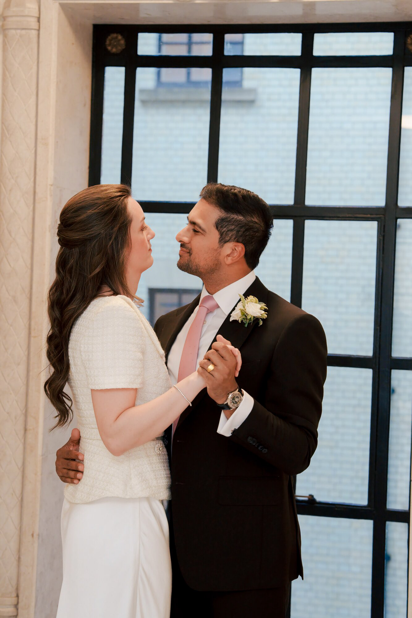 Bride and groom slow dancing by a tall window inside Old Marylebone Town Hall