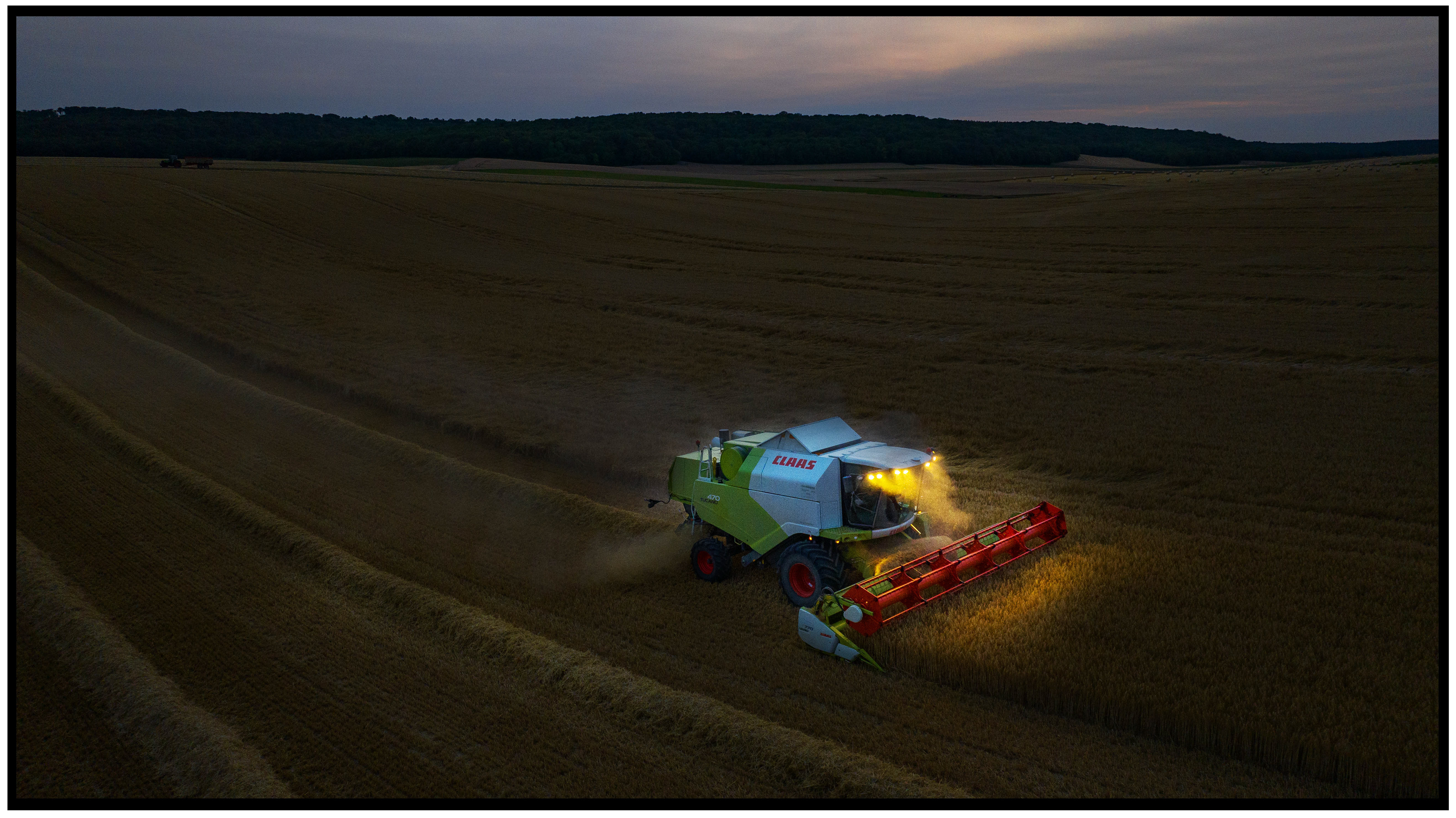 Moissonneuse opérant de nuit avec ses phares allumés, symbole du travail sans relâche des agriculteurs qui doivent récolter avant un changement de météo imminent.