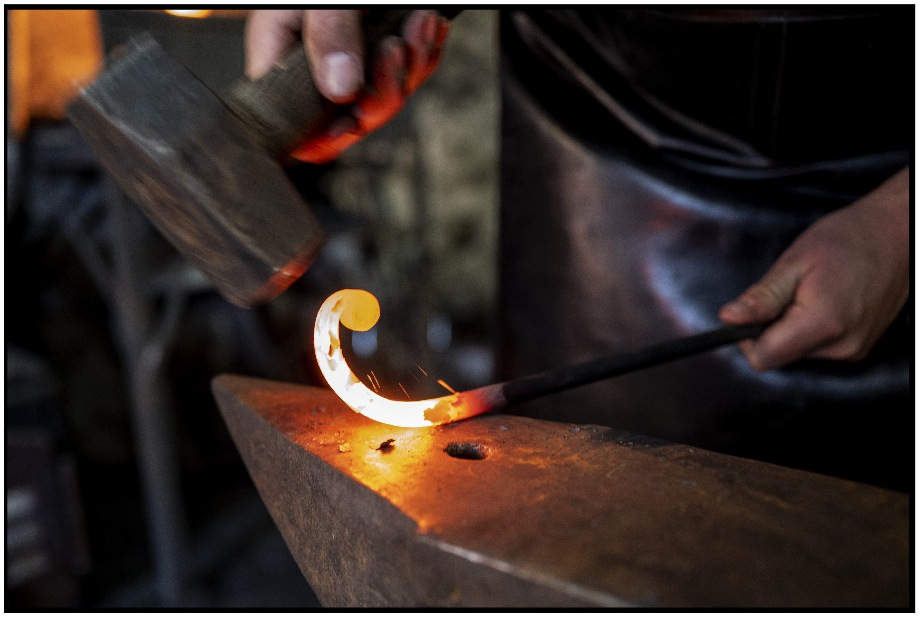 Forgeron en plein mouvement, frappant le métal avec un marteau, illustrant la force et le savoir-faire du métier.