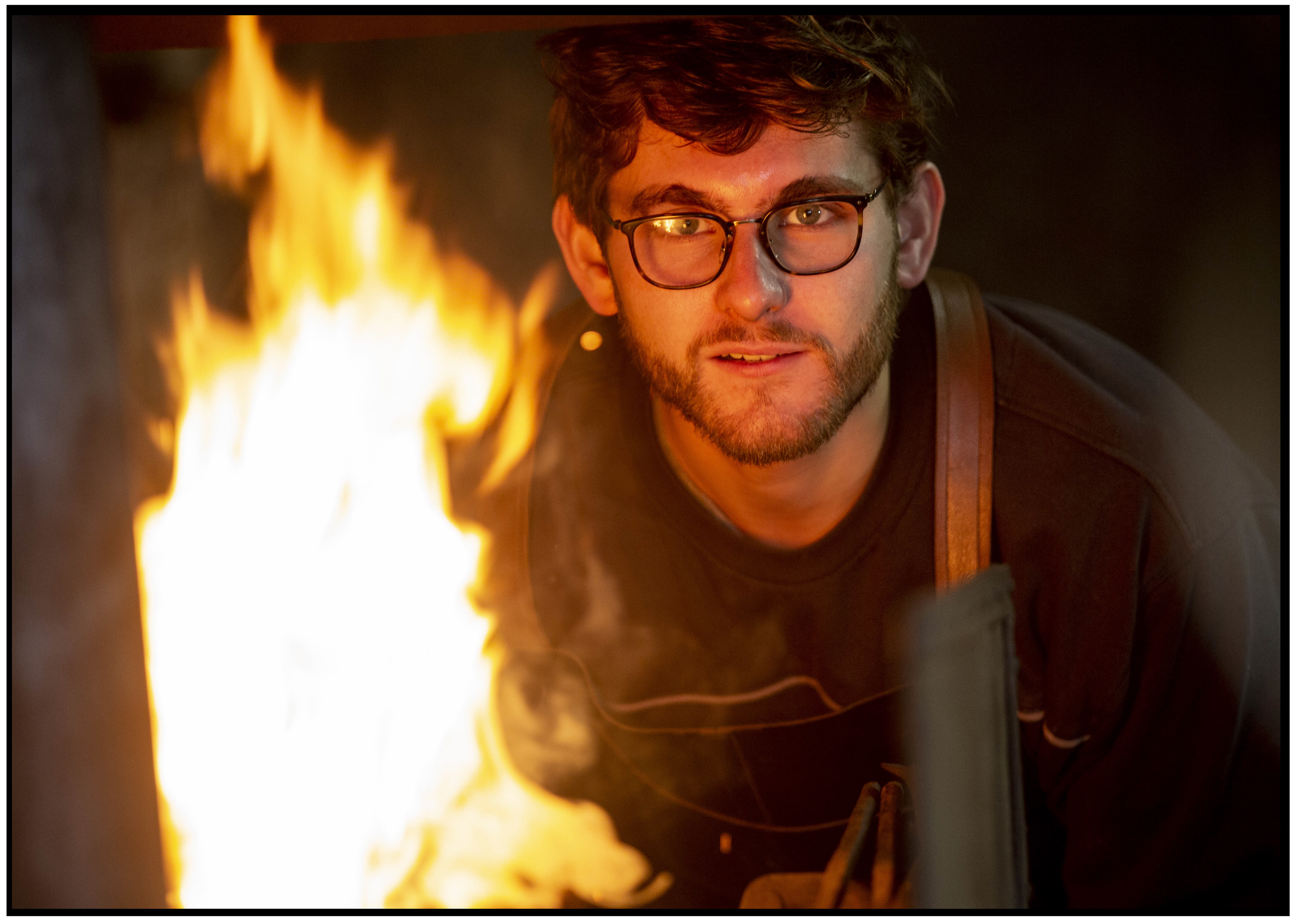 Jeune forgeron observant le feu de la forge, animé par la passion du fer et du feu.