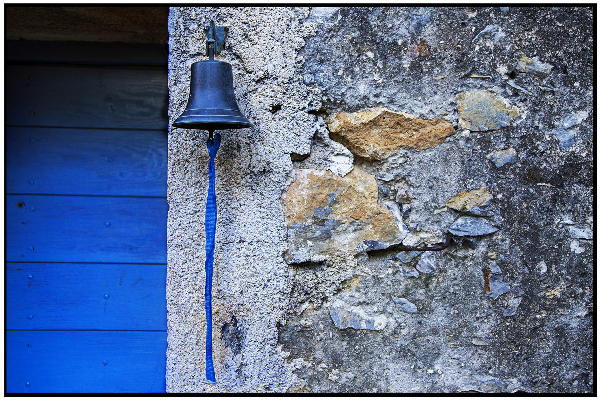 Porte bleue avec une cloche dans la vallée de la Roya, entourée d'un mur en pierre.