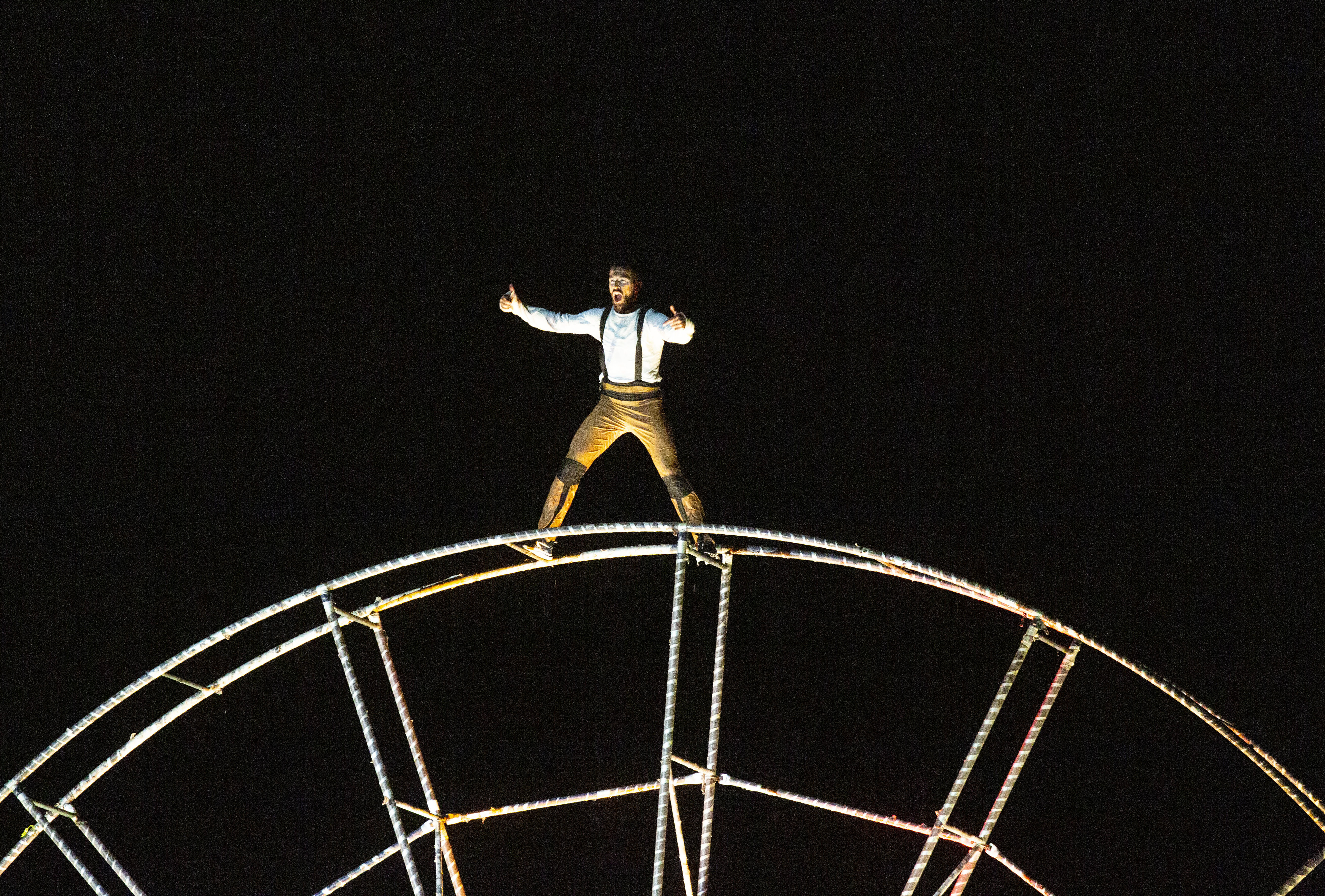 Artiste jongleur se tenant au sommet de la grande roue, illuminé par les lumières de la nuit.