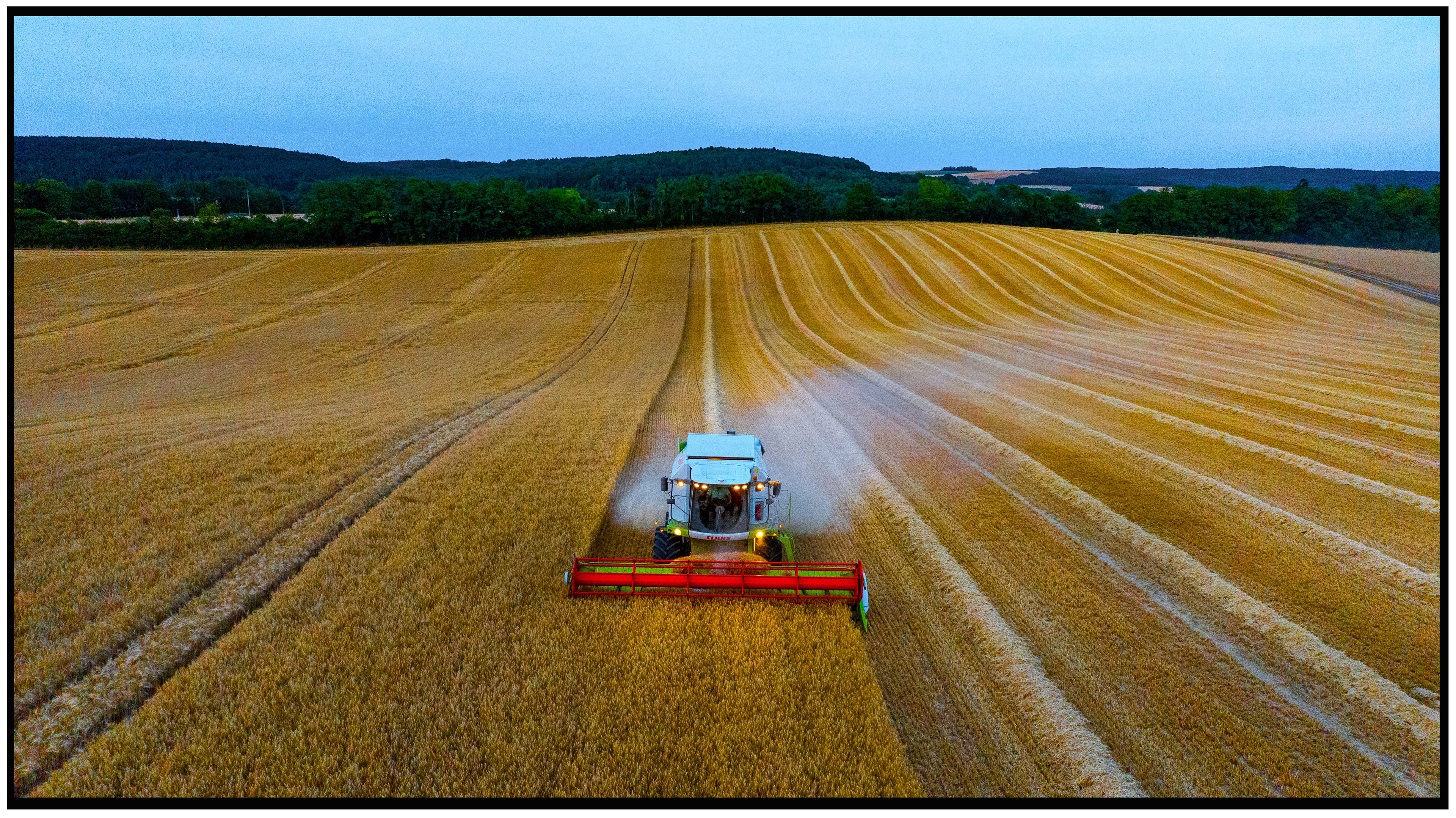 Une moissonneuse moderne tracant des lignes colorées dans un champ, créant des motifs presque artistiques dans la terre.
