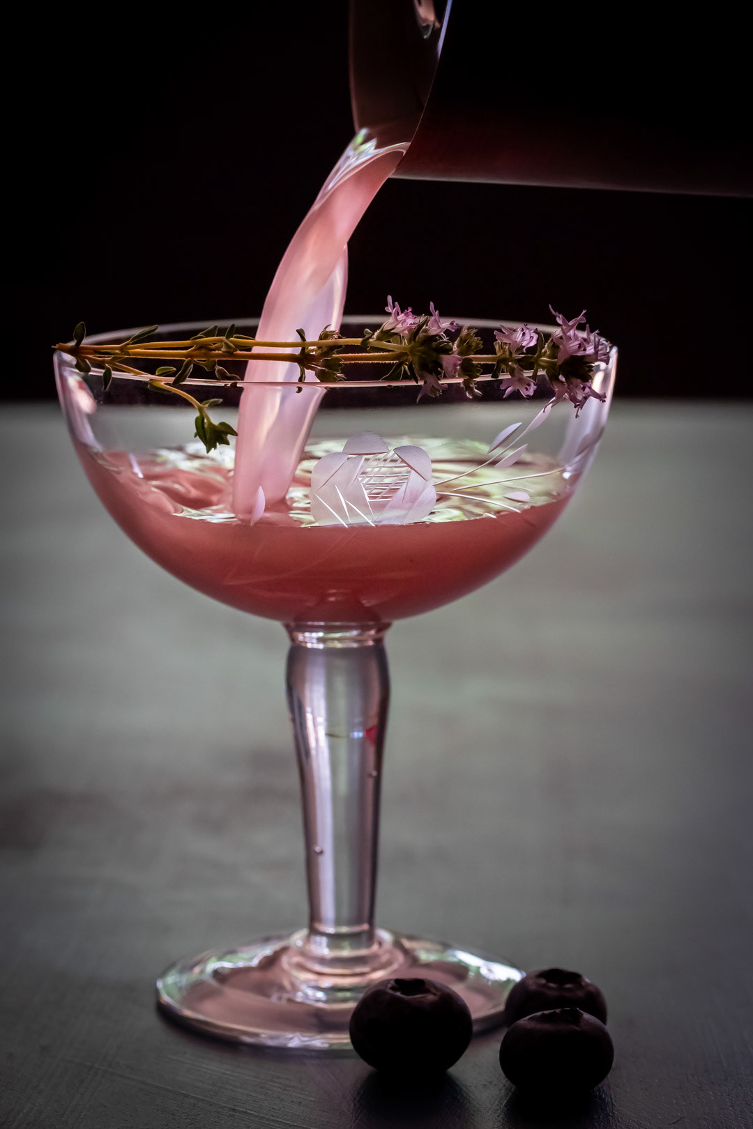 pouring a blueberry shrub pisco sour with purple thyme flower garnish