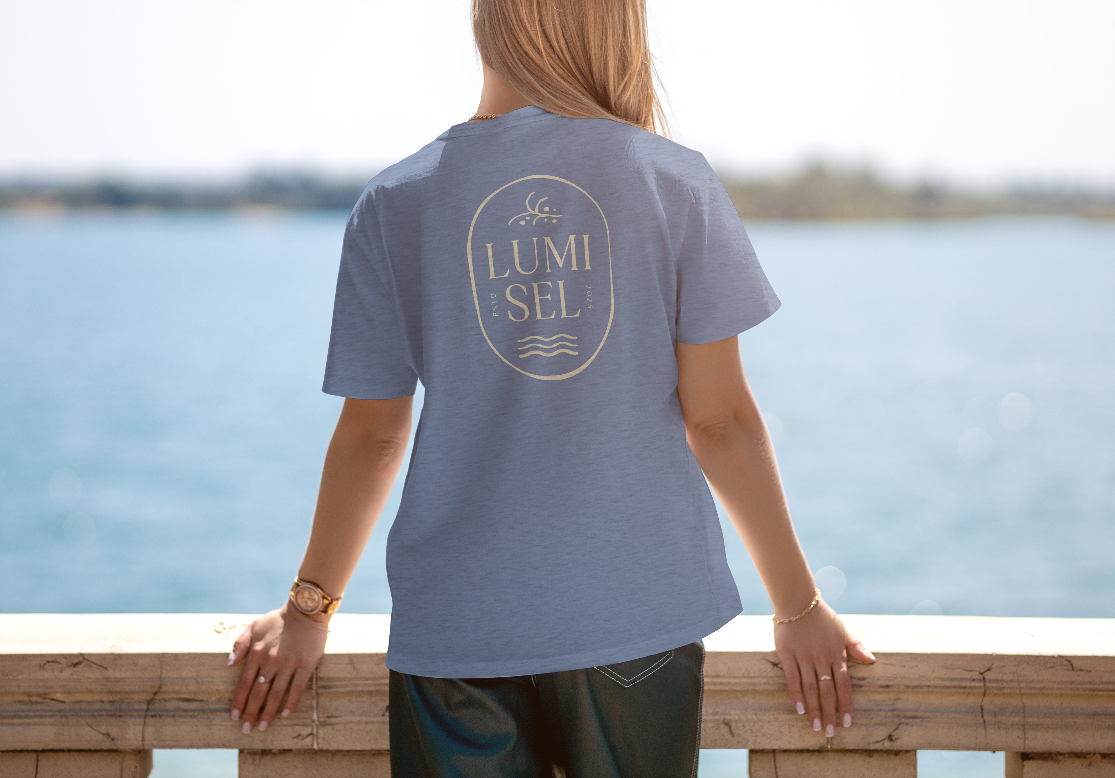 Woman overlooking the beach, with a blue shirt with the back of the shirt showing the vertical variant of the logo