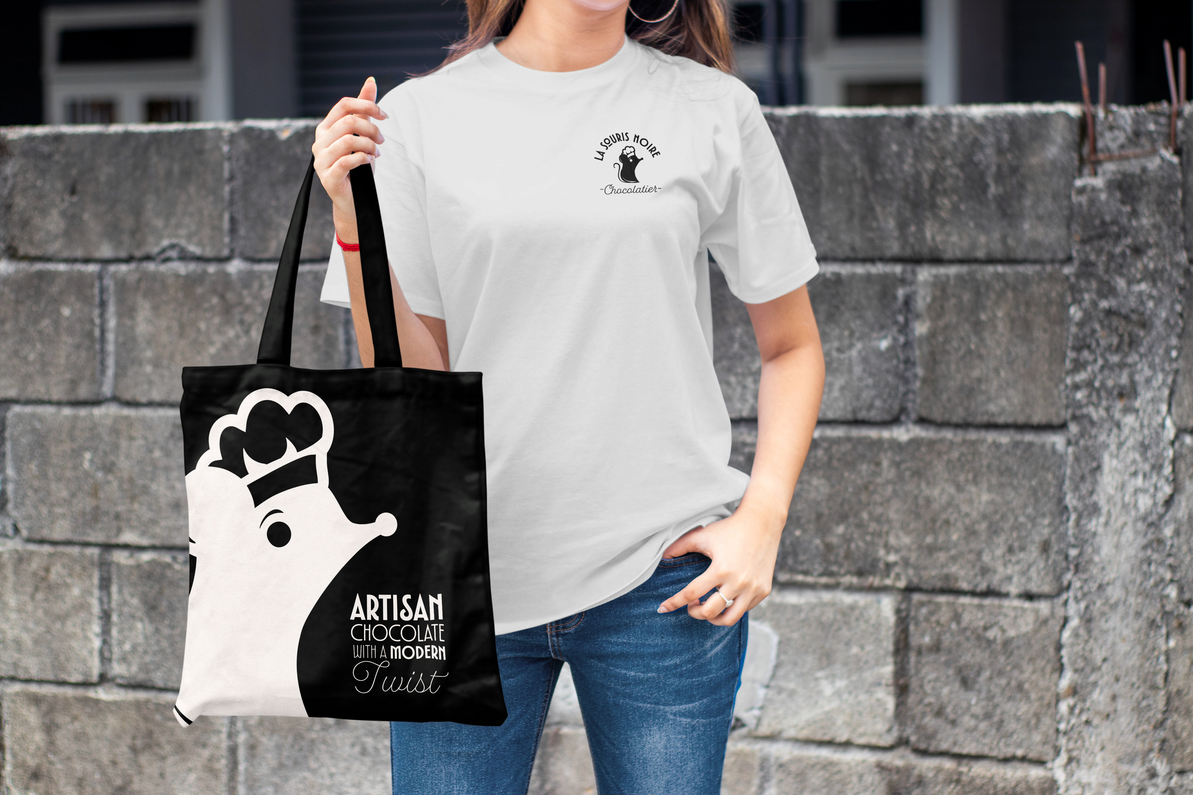 Mockup of a Woman holding a tote bag with the mouse logo enlarged and text. The woman is wearing a white t-shirt with an alternative logo design