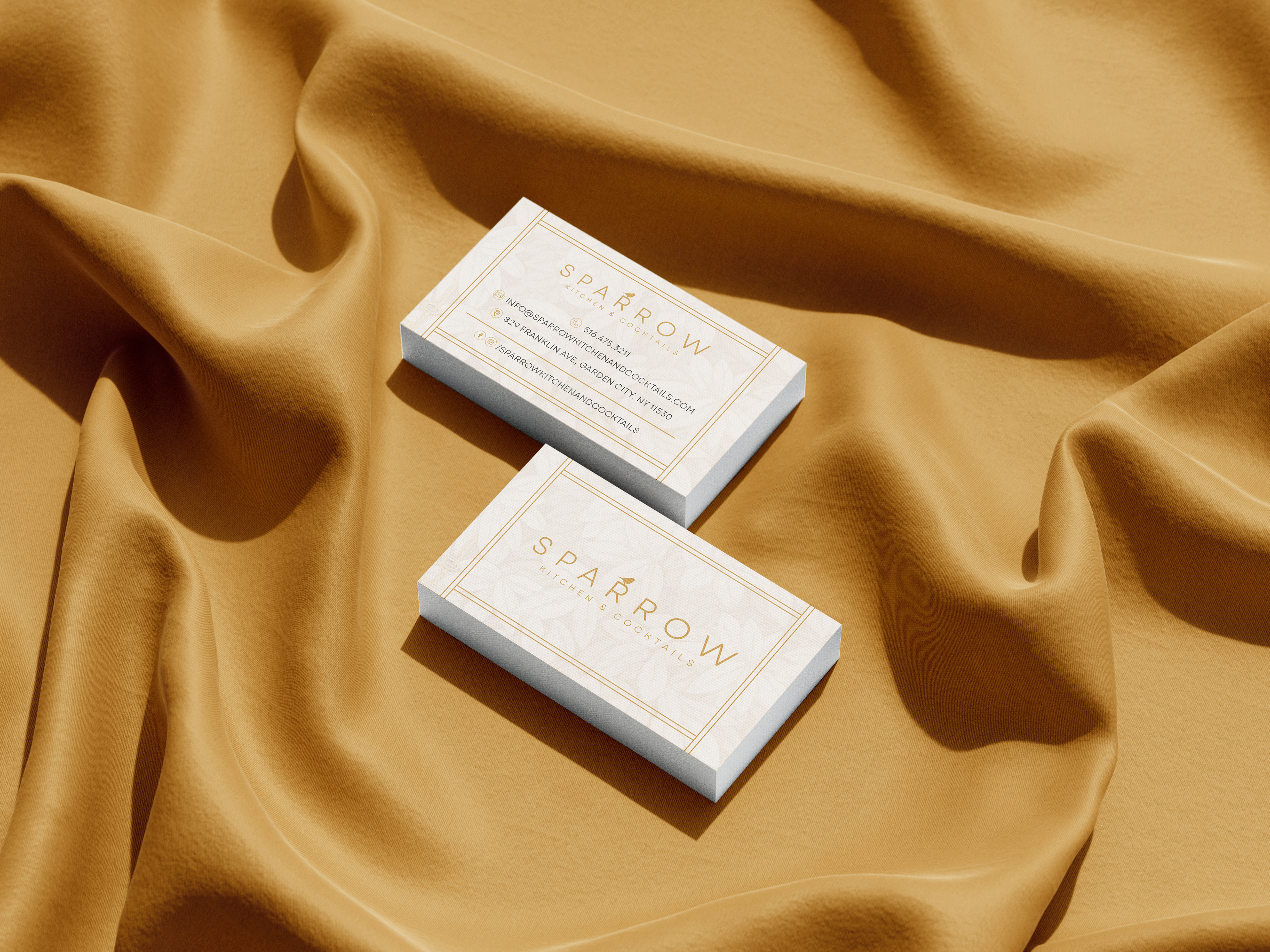 Minimalist gold and white Sparrow Kitchen & Cocktails business card design shown in elegant flat lay on golden cloth