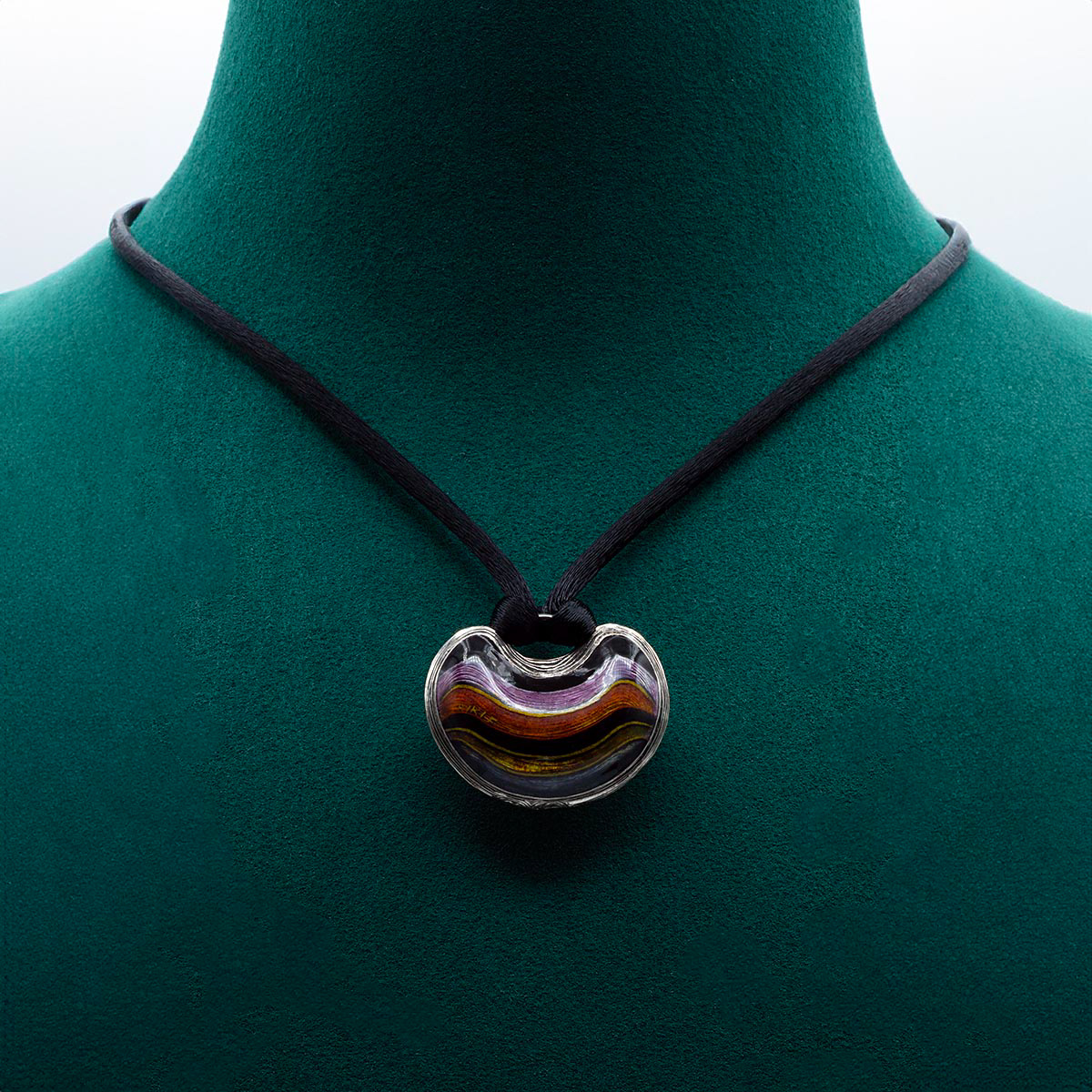 Collier LES PENDELOQUES P002 rayé en argent, avec un pendentif gravé à la main et émaillé, affichant un motif rayé violet, rose, jaune et noir. Conçu avec la technique de l'émail champlevé, complété par un collier en soie noire avec fermoir en argent 925/1000 et une zircone cubique de 1,5 mm. Bijou fait main en édition limitée par Kiki Fornell.