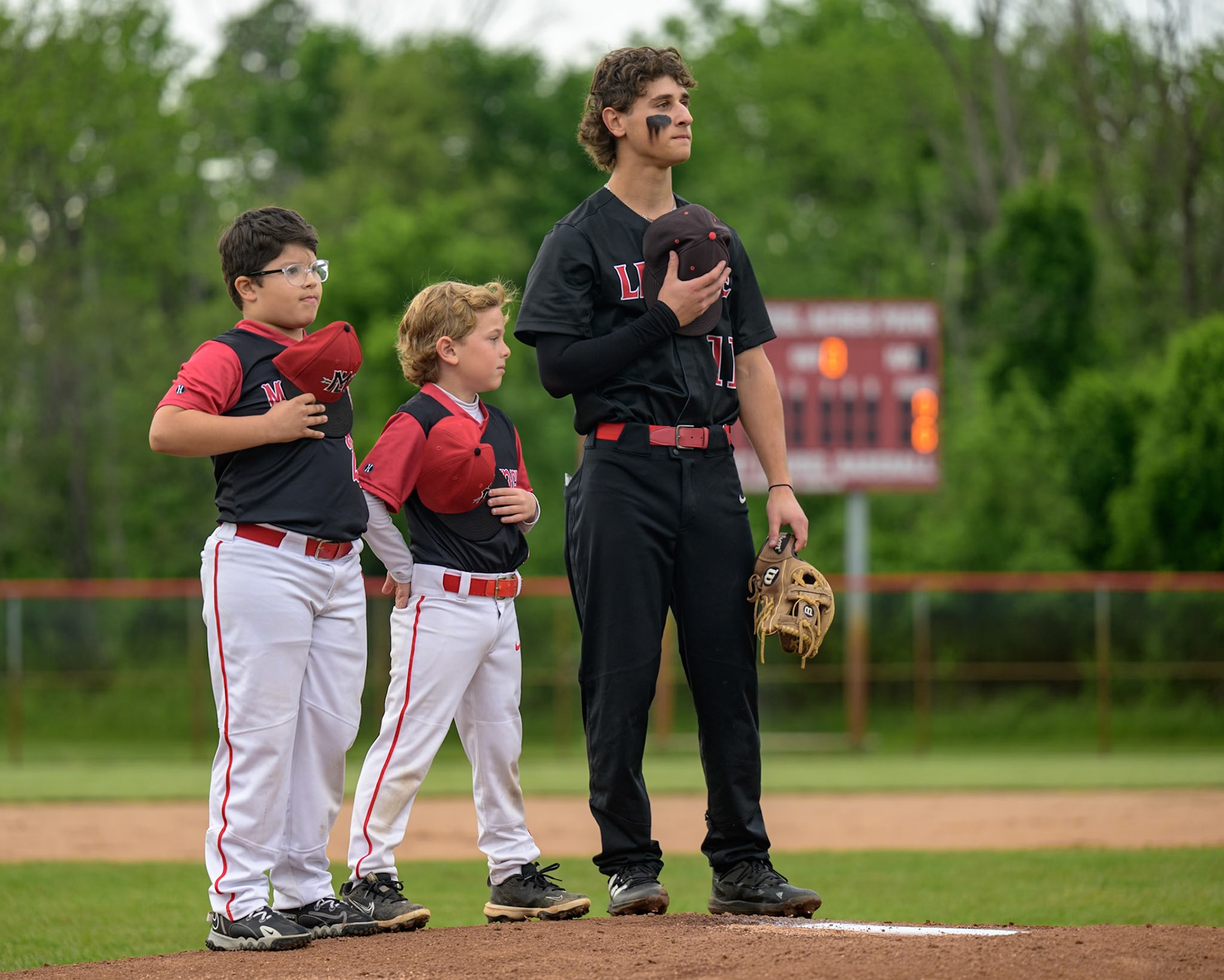 Michael Kahn of Lenape High School and members of the Mount Laurel 8u baseball team stand for the National Anthem prior to the matchup between the Lenape Indians and the Cherry Hill East Cougars at Mount Laurel Baseball Night at Laurel Acres Park in Mount Laurel, NJ. Lenape went on to win the game 10 - 0. (Photo by Brian Barbash/gametimedreams.com)