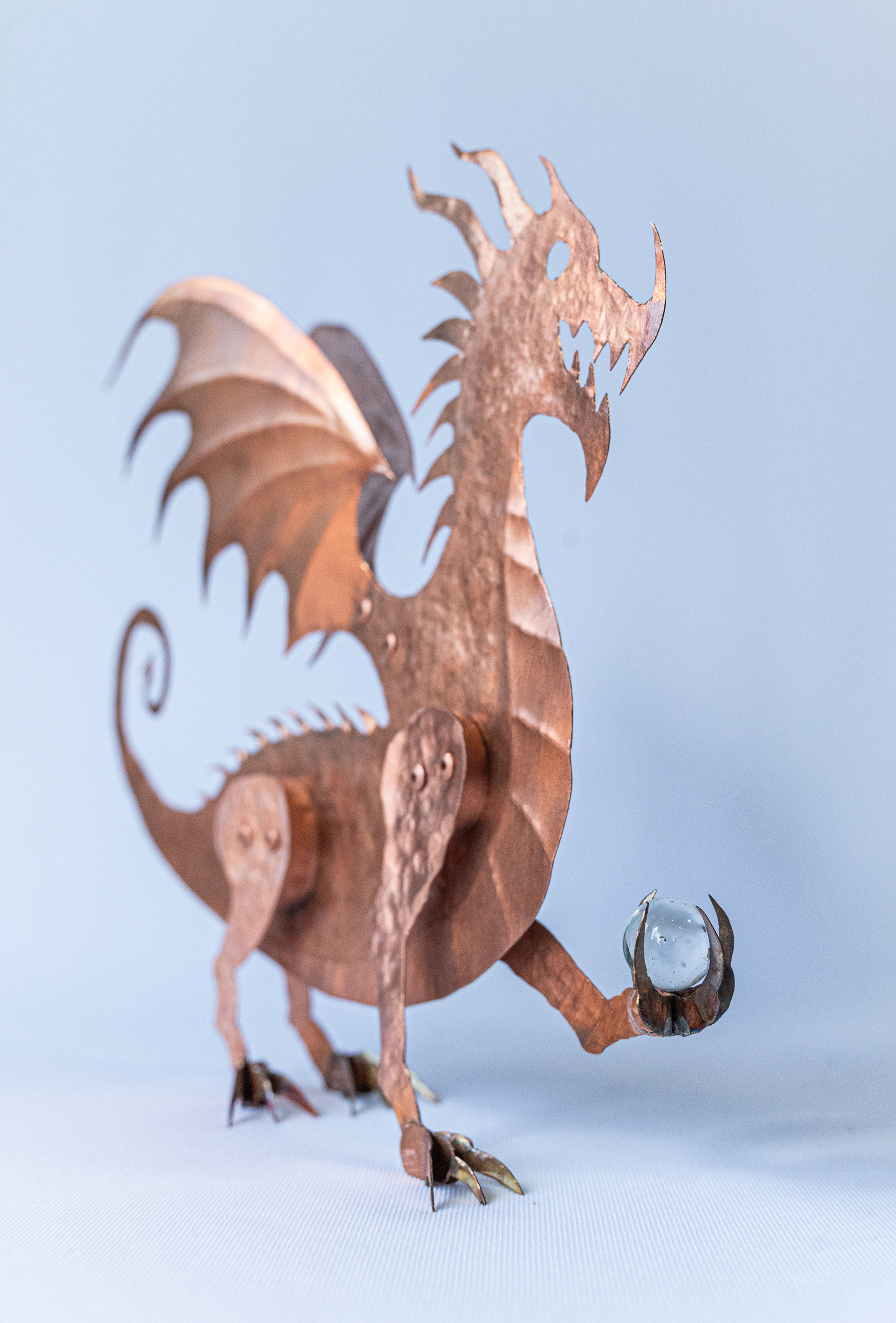 This amazing one of a kind Dragon is a unique and original design by Marty Borsboom. Hand cut from a sheet of copper, it is hand hammered and embossed and holds a glass marble. It stands at 9 inches high  x 7.5 wide and 2 inches deep. $175