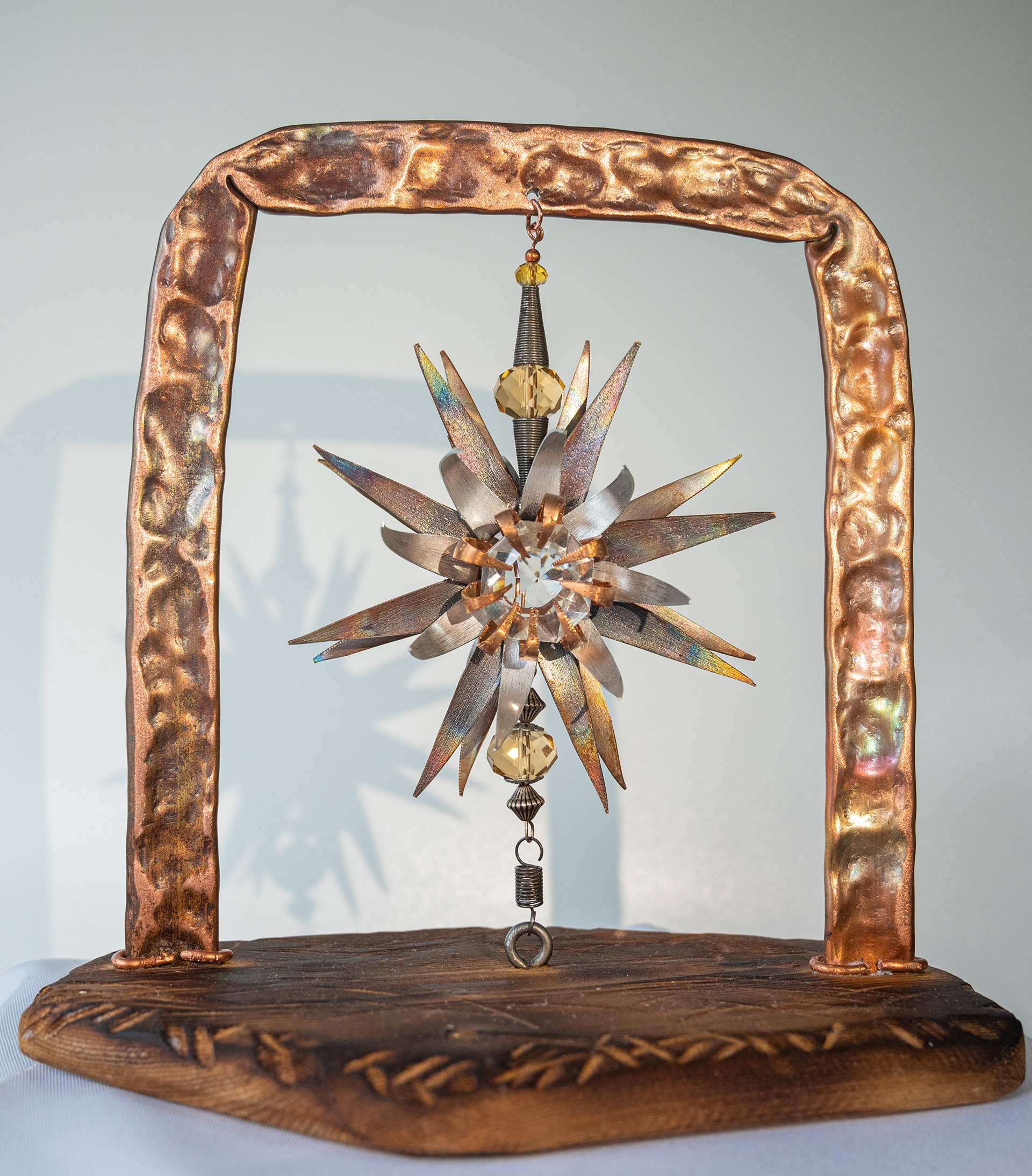 "Rotations". This copper flower with a clear crystal centre can spin on its axis, held between a hammered copper frame and fir base. 8.5 inches wide x 9 inches high x 5.5 inches deep, $125