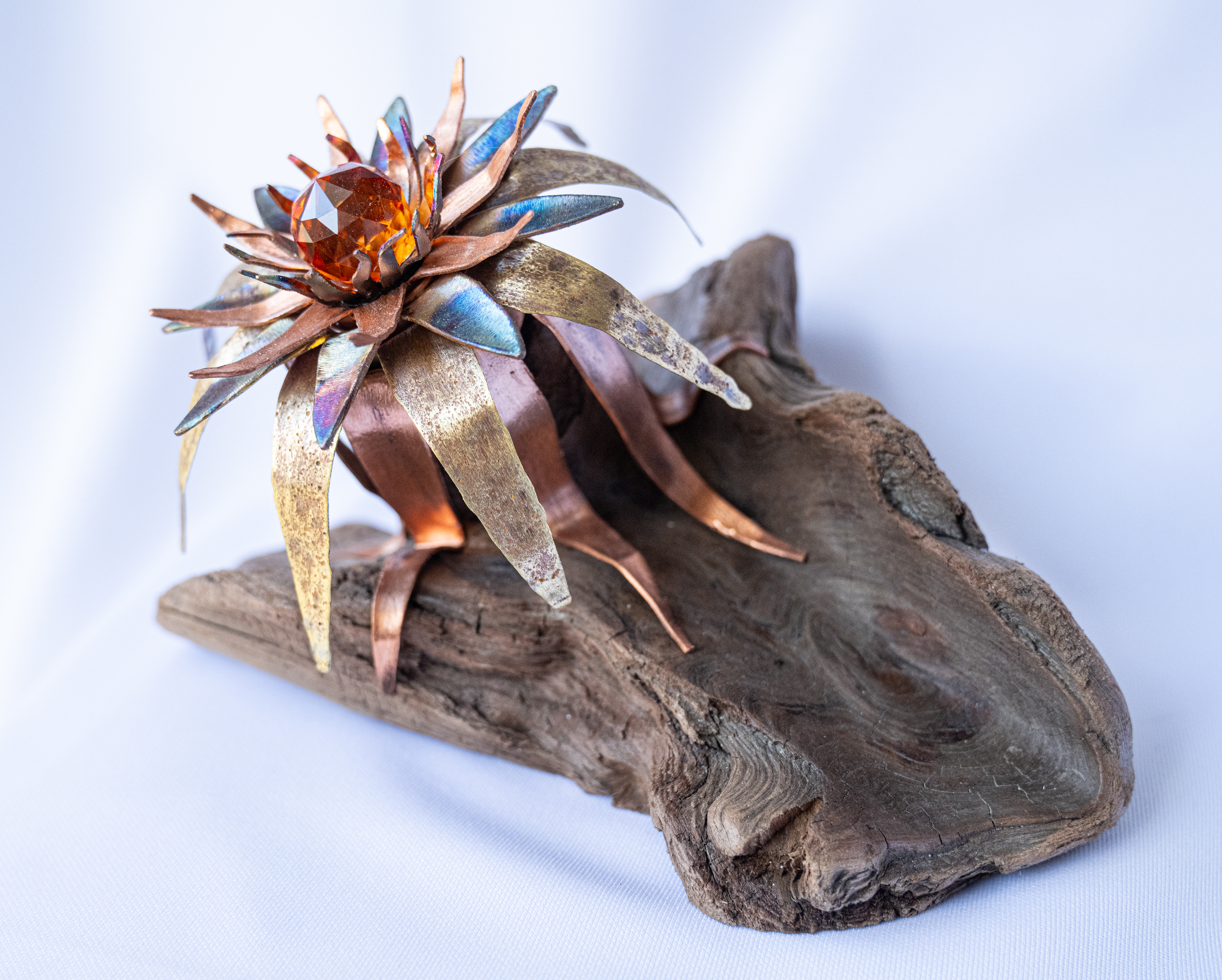 "Madeleine",  8.5 x 6 x 5.25, has a copper and brass flower with an orange crystal centre and is mounted on Vancouver Island driftwood, $175
