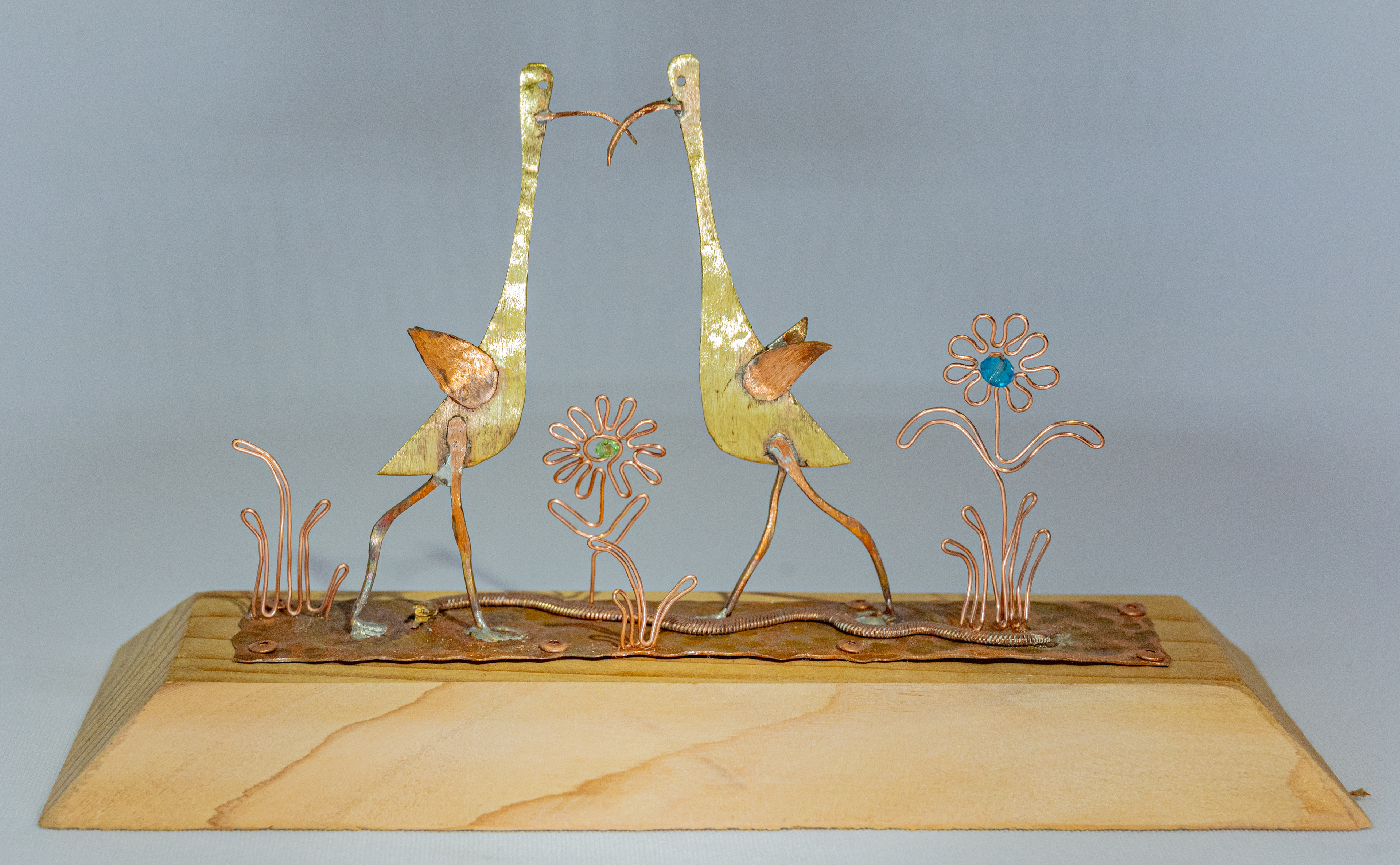 "Lovebirds" are brass and copper birds, copper wire flowers with glass crystal centres on a hammered copper strip with a copper bracelet snake slinking through the grass on a cedar base,  9 inches wide x 3.5 inches deep x 5 inches high, $75