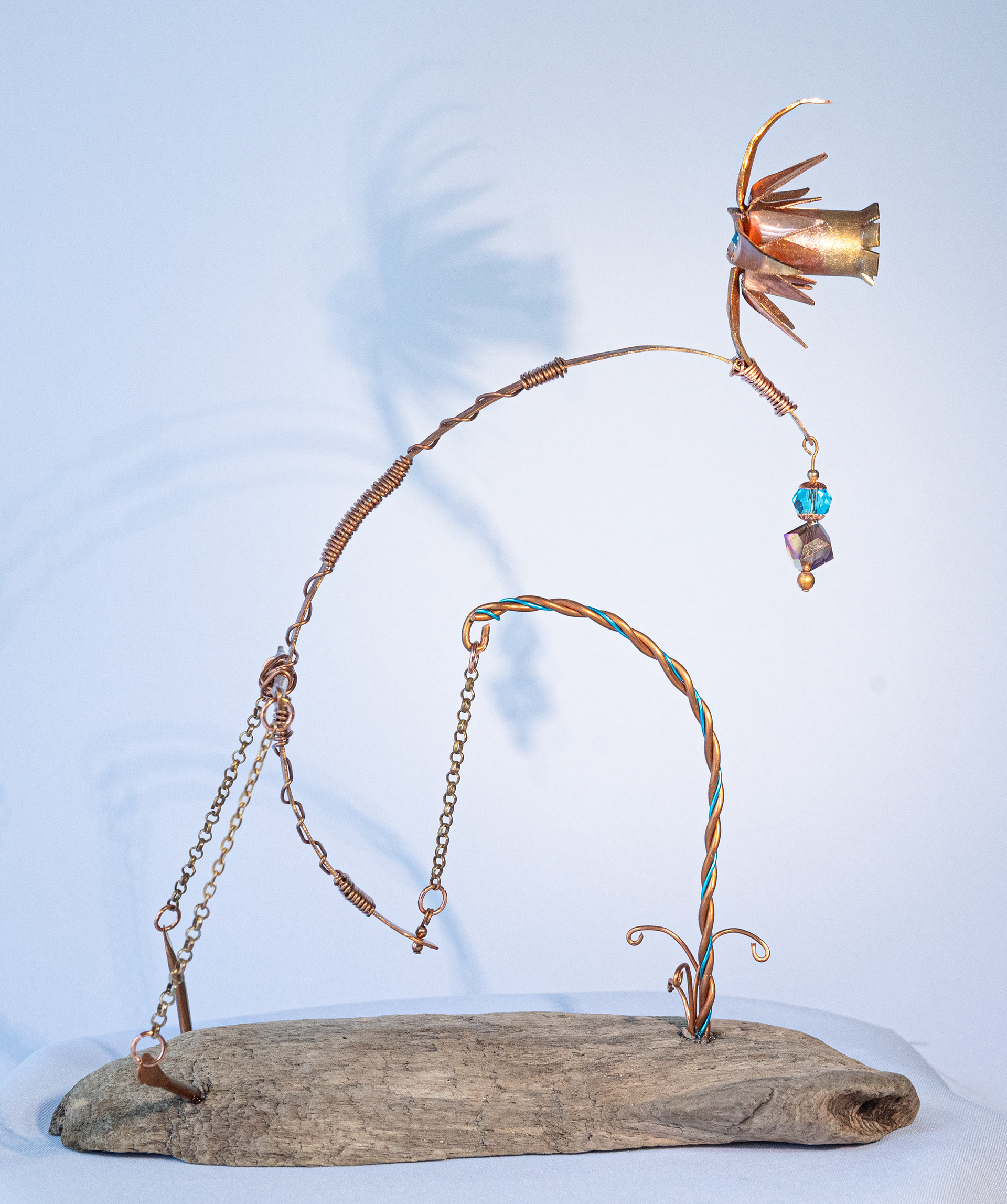 "Weightless" (side view) features a gravity held copper and aluminum flower with copper stem, hand twisted wire, brass chain, iridescent and blue crystals on a driftwood base, 10 inches high x 8 inches wide x 4 inches deep, $175