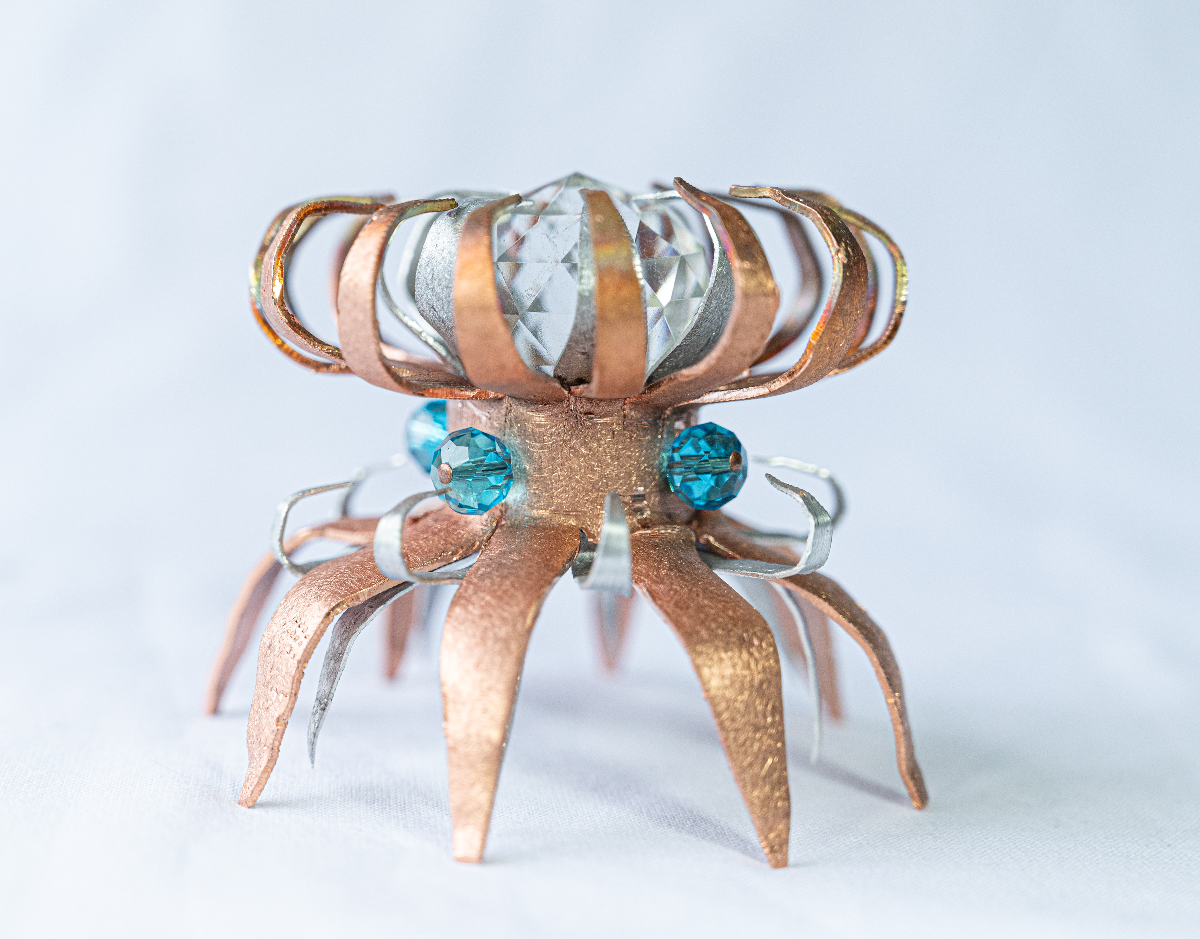 "Anemone" (side view) is a hand-formed copper and aluminum creation. It holds a 1.25" clear crystal in its tentacles and is embellished with turquoise crystals around the centre. It measures 3" in diameter and is 3" high, $75