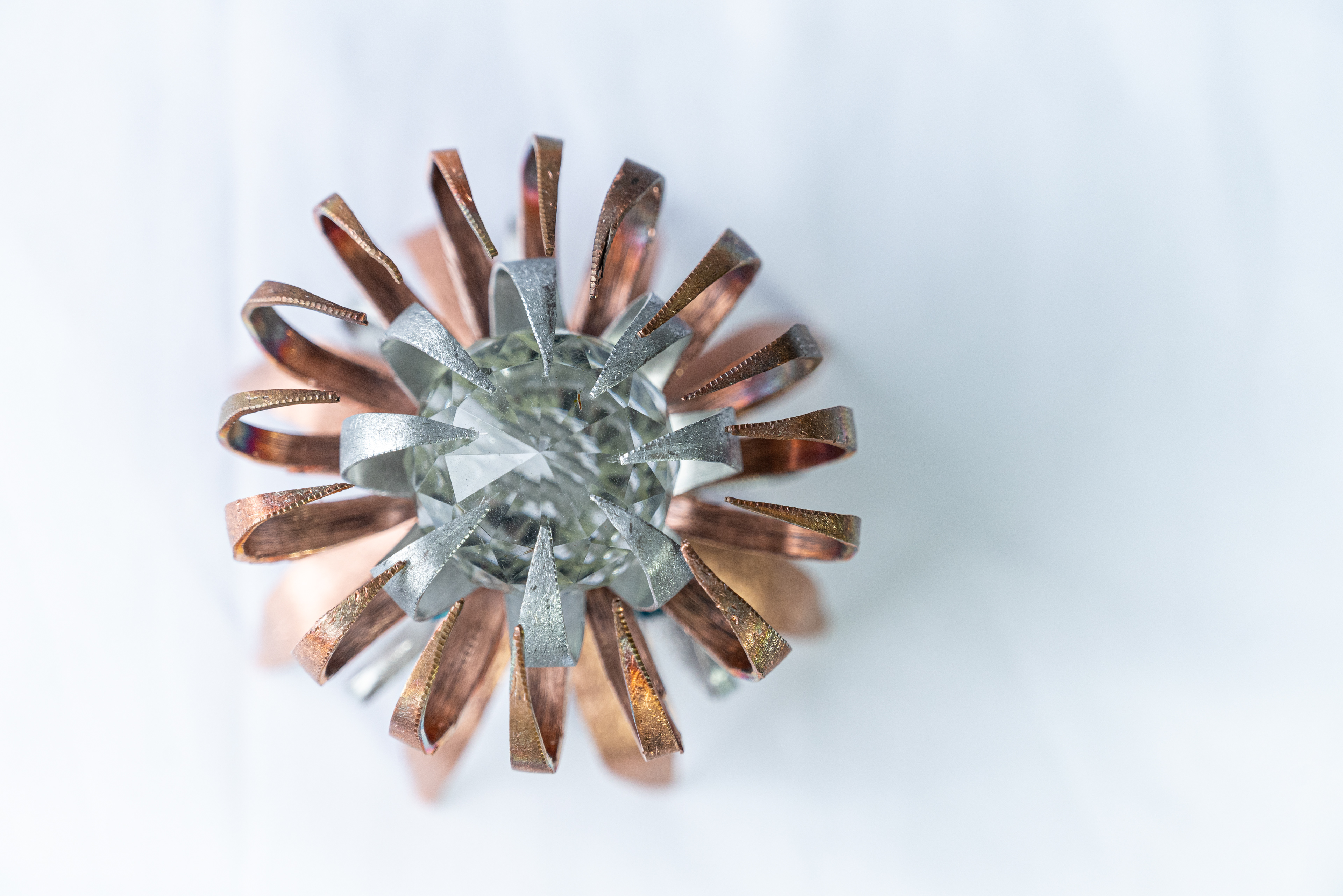 "Anemone" (overhead view) is a hand-formed copper and aluminum creation. It holds a 1.25" clear crystal in its tentacles and is embellished with turquoise crystals around the centre. It measures 3" in diameter and is 3" high, $75