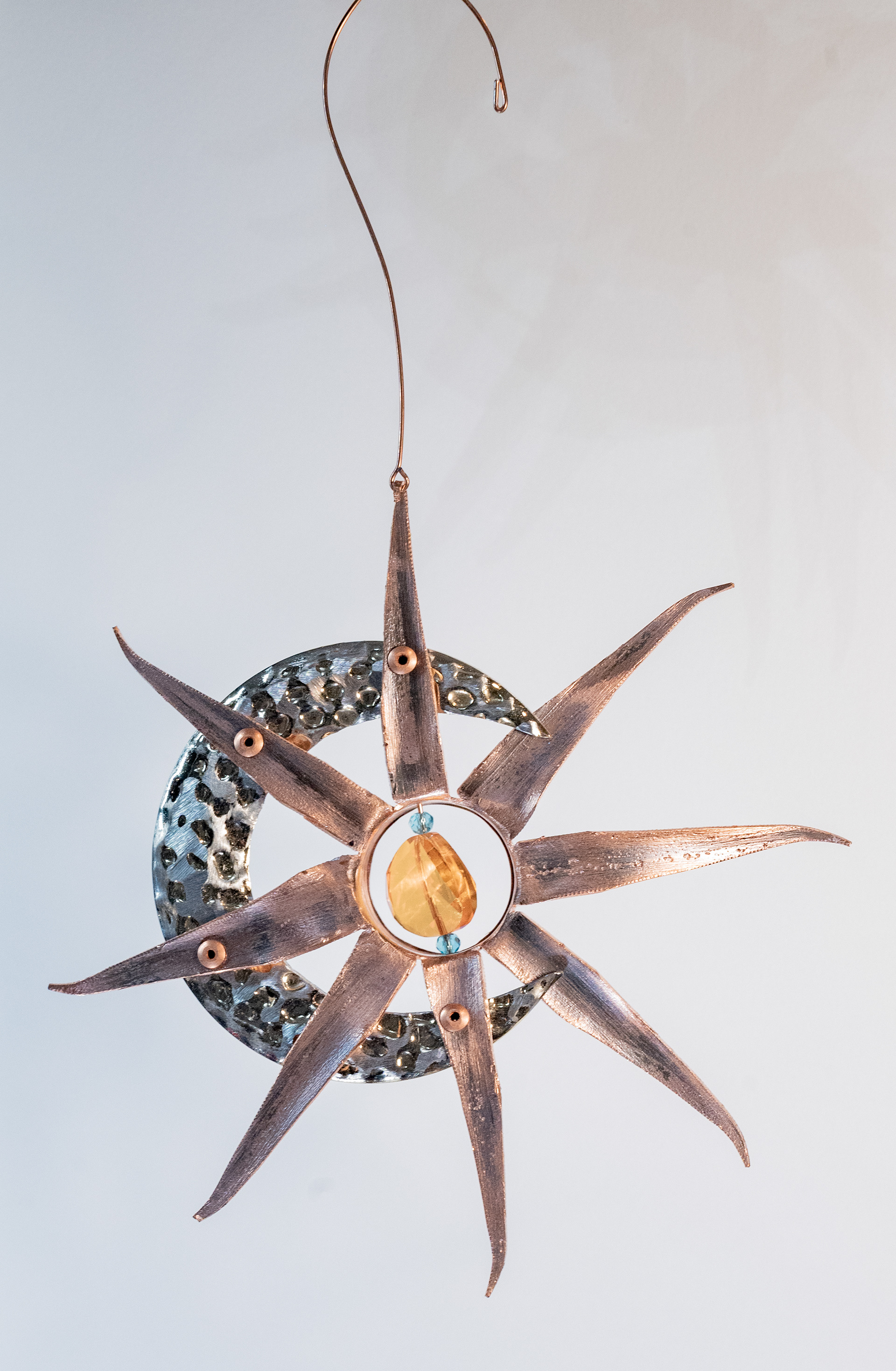 "Moon and Sun" is made with a handcut copper sun riveted onto a mixed metal crescent moon with amber and turquise crystal accents, $75
