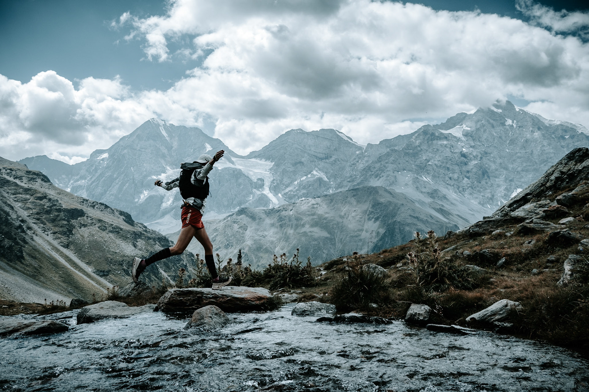 A trailrunner jumping in front of Ortler and Königsspitze