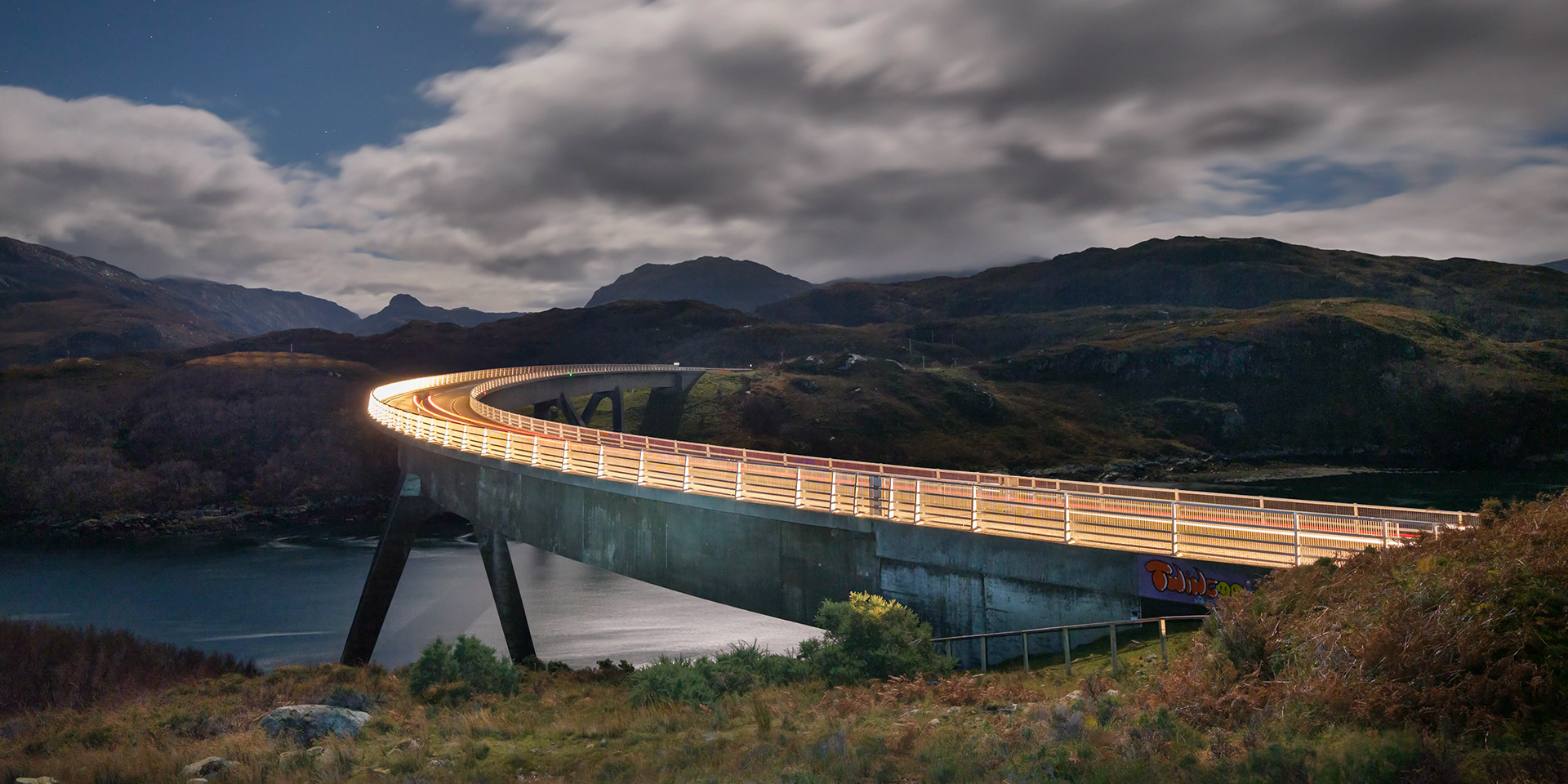 The Kylesku Bridge, lit up by the headlights of a single passing car.