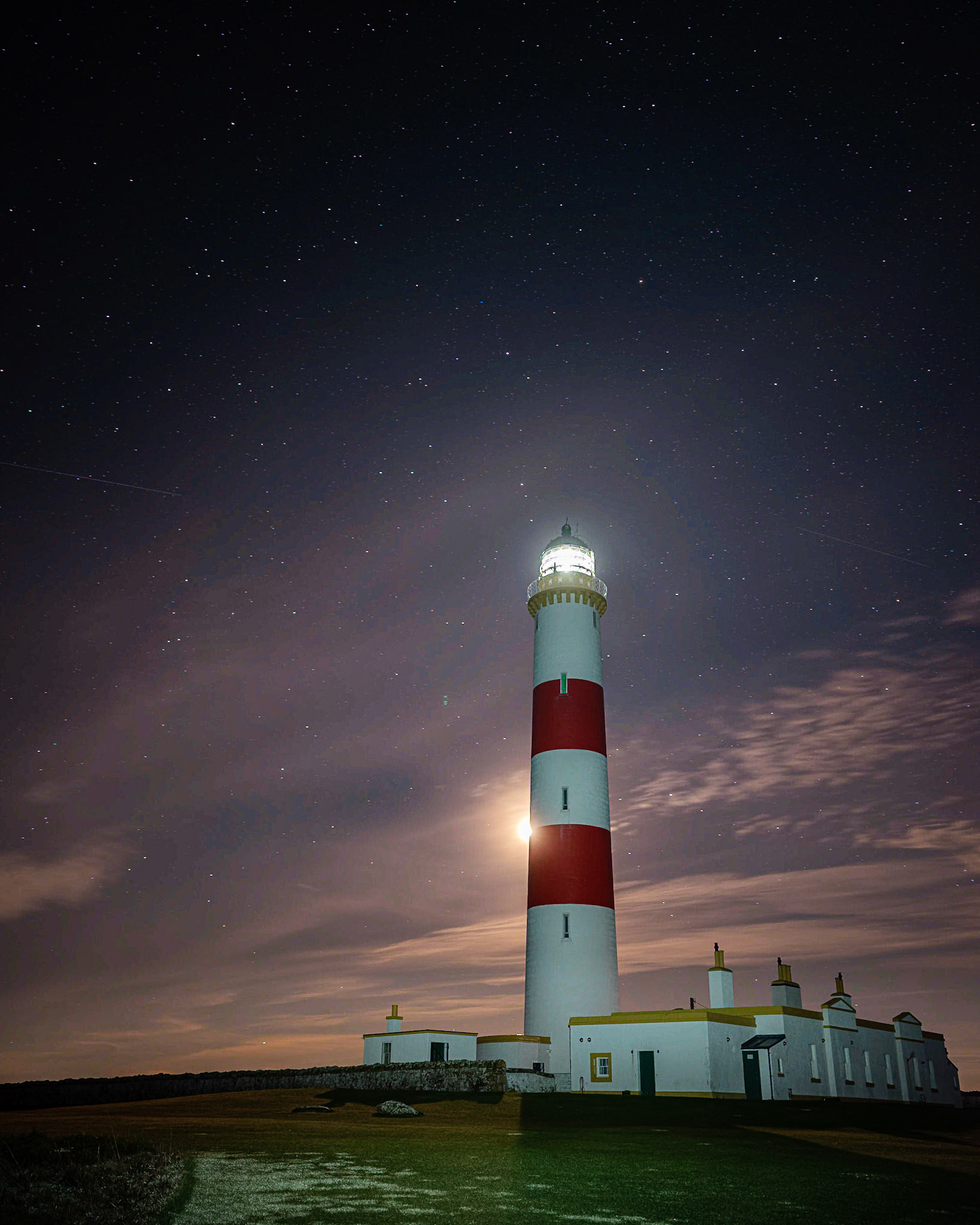 The moon peeks from behind Tarbatness Lighthouse.