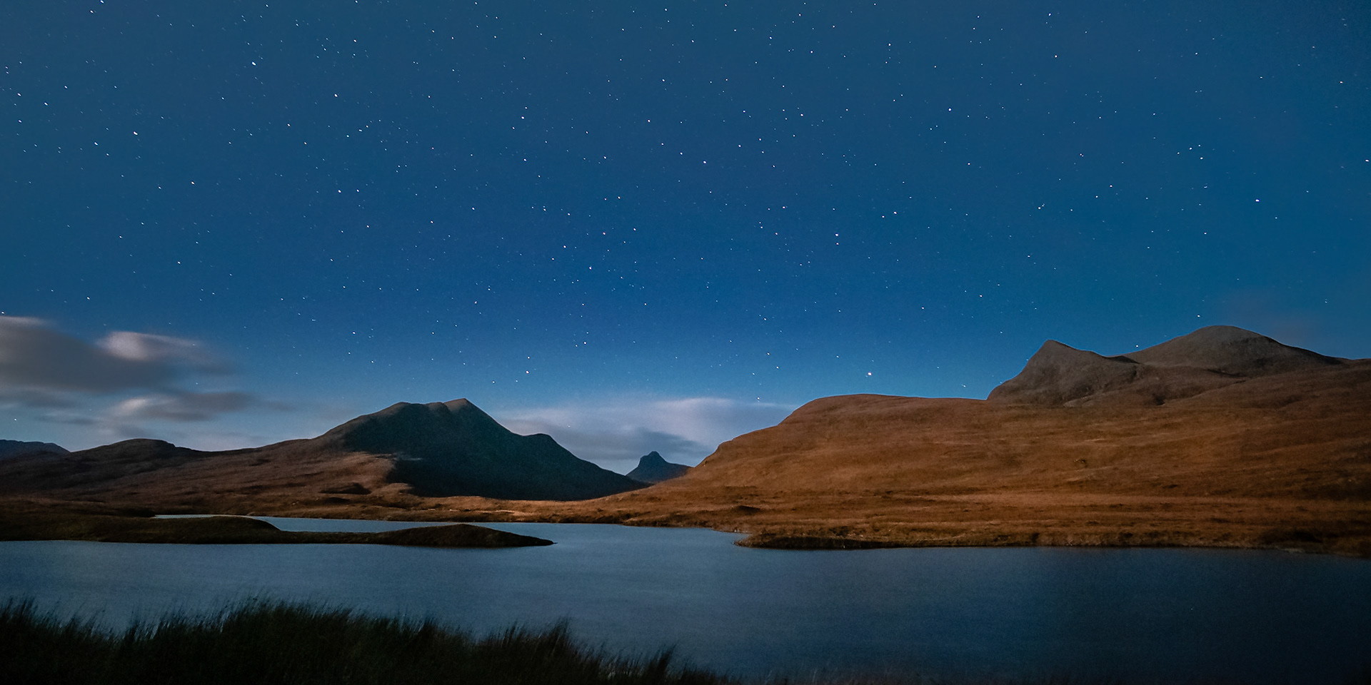 Stac Pollaidh peeks between the mountains of Coigach in Scotland's North West Highlands on a clear, moonlit night.