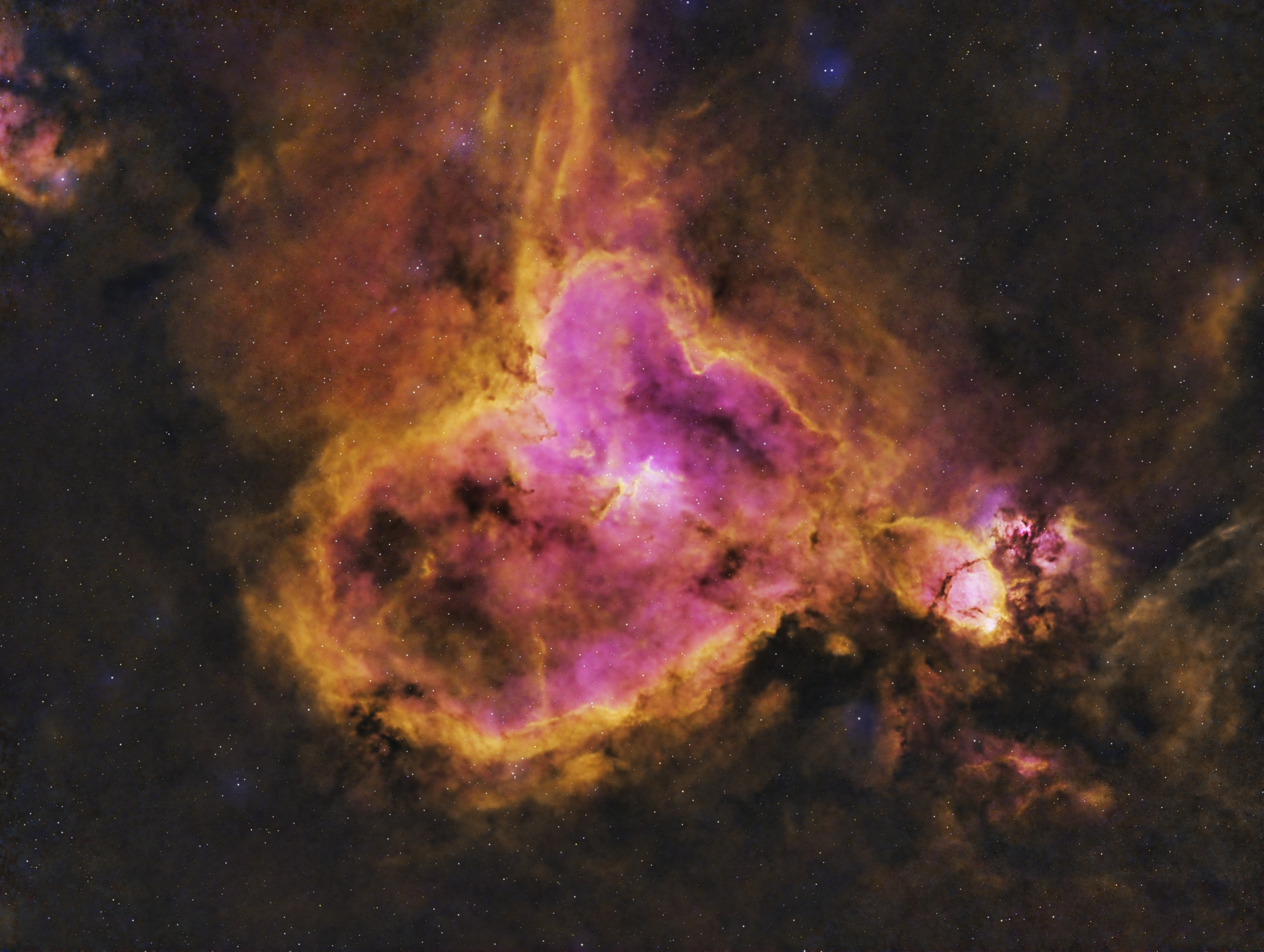 The Heart Nebula is an emission nebula located in the constellation Cassiopeia. It displays glowing ionized hydrogen gas and darker dust lanes, pinkish in the image. It is also made up of ionised oxygen and sulfur gasses, contributing the blue and orange colors. The shape of the nebula is driven by stellar winds from the hot stars in its core.  Distance: 7500 light years Radius: 165 light years