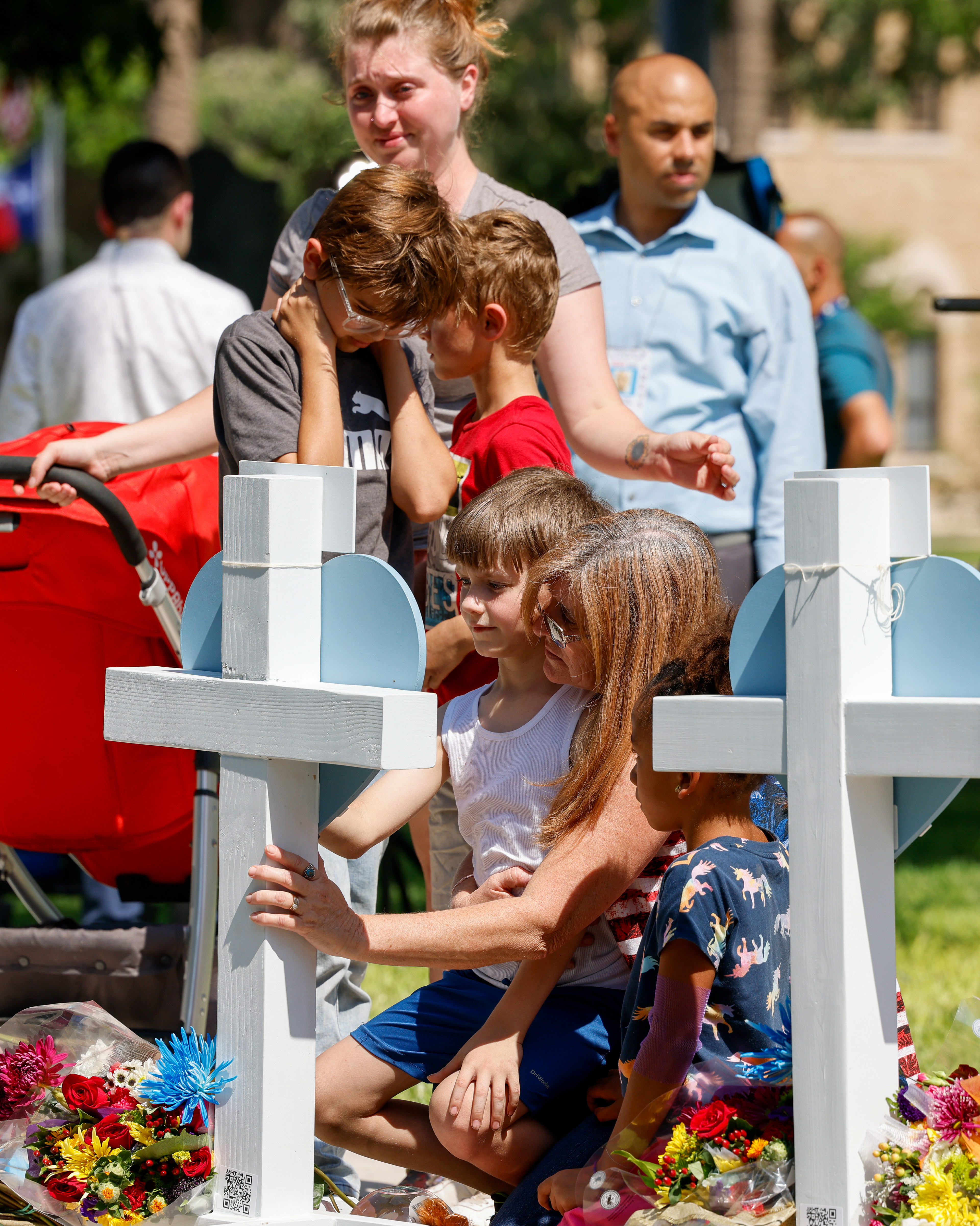 Angela Turner, 49 (bottom right), comforts her nephew Bruce Mathis, 8, at a cross for his sister Maranda Mathis, 11, who was killed in the Robb Elementary School Shooting at the town square in Uvalde, Texas, Thursday, May 26, 2022.