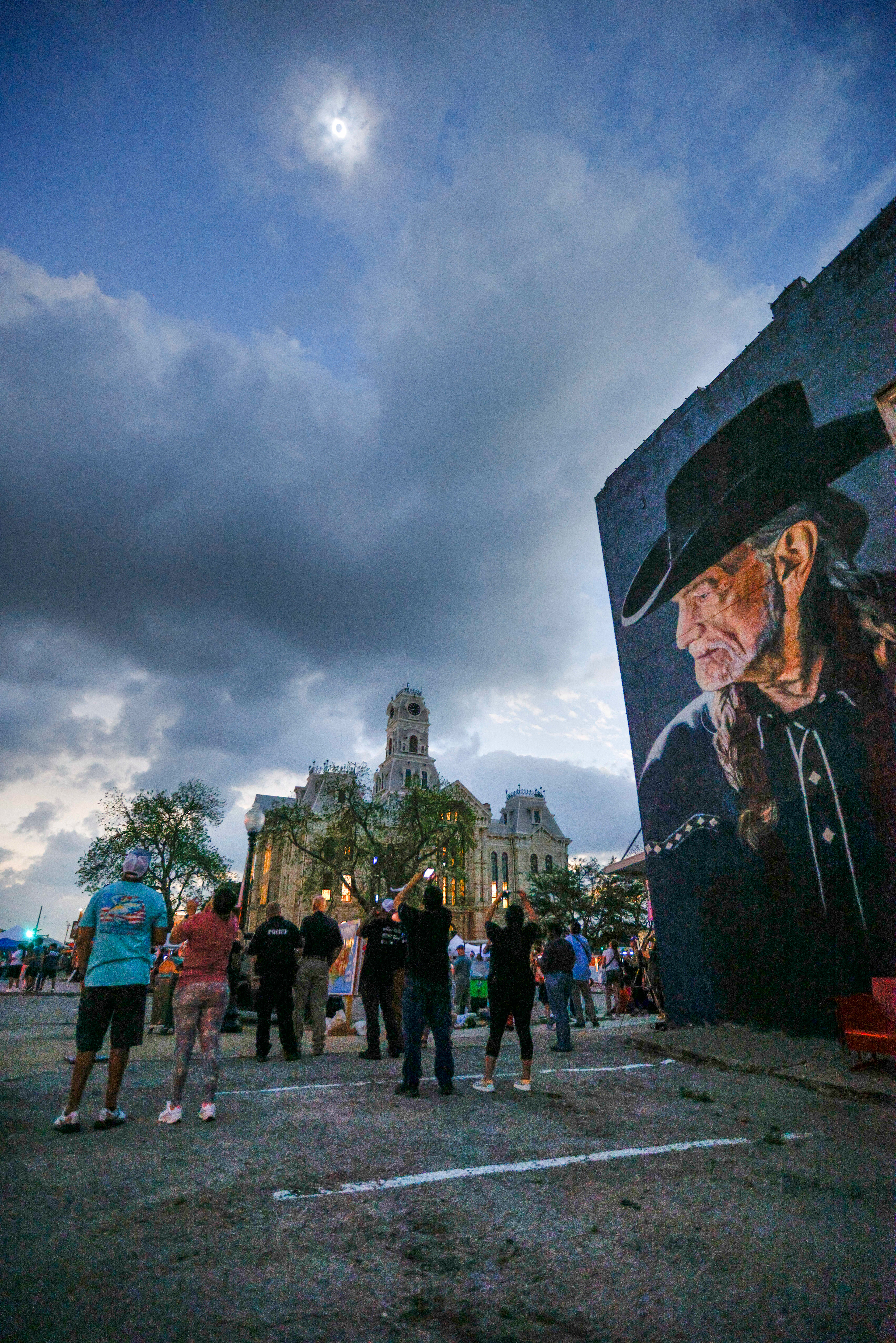 People watch a total solar eclipse over the Hill County Courthouse and a mural of Willie Nelson in downtown Hillsboro, Texas, Monday, April 8, 2024.