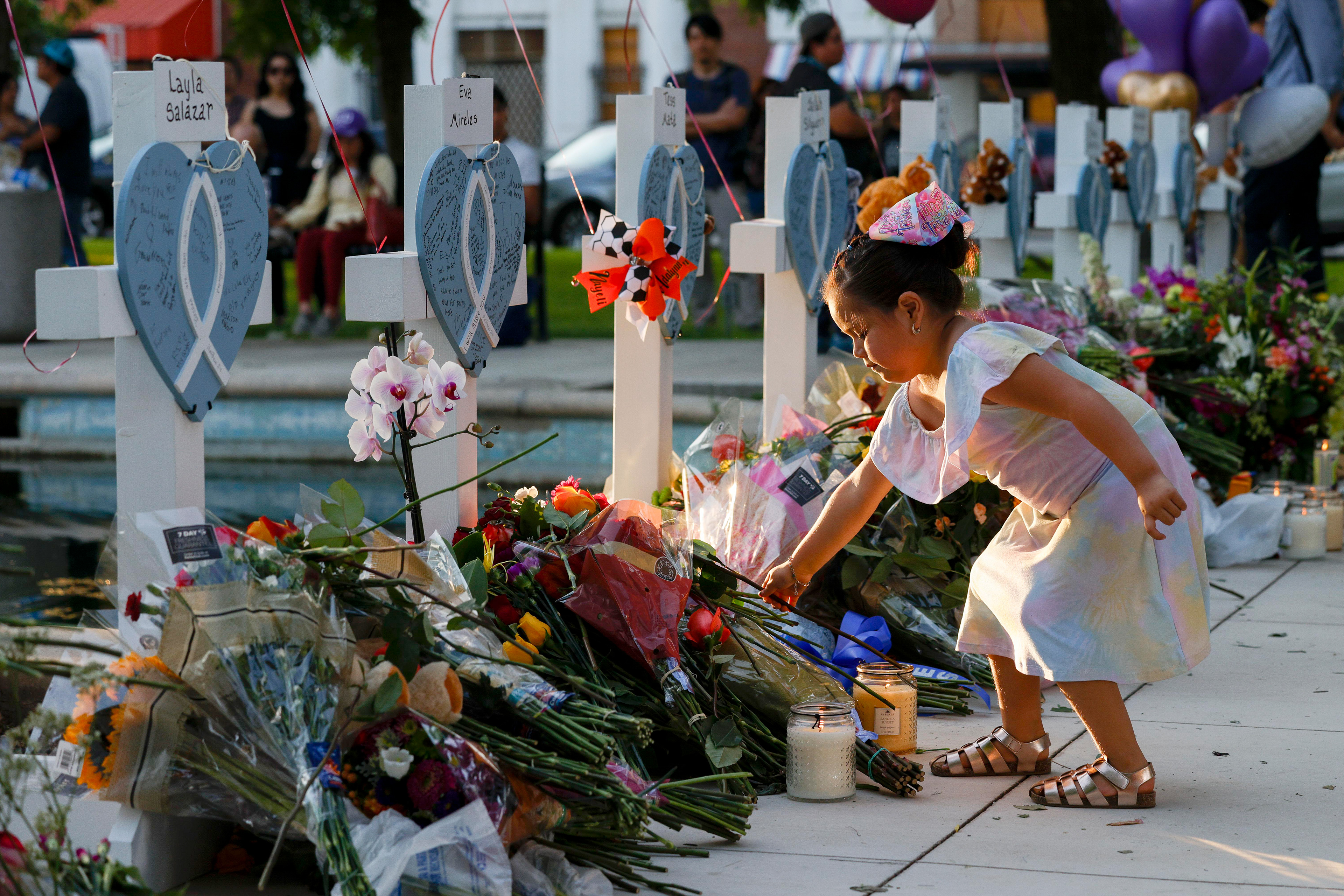 Four-year-old Bella Cazares lays a rose at a cross for fourth grade teacher Eva Mireles alongside a memorial for the victims of the Robb Elementary School shooting at the town square in Uvalde, Texas, Thursday, May 26, 2022.