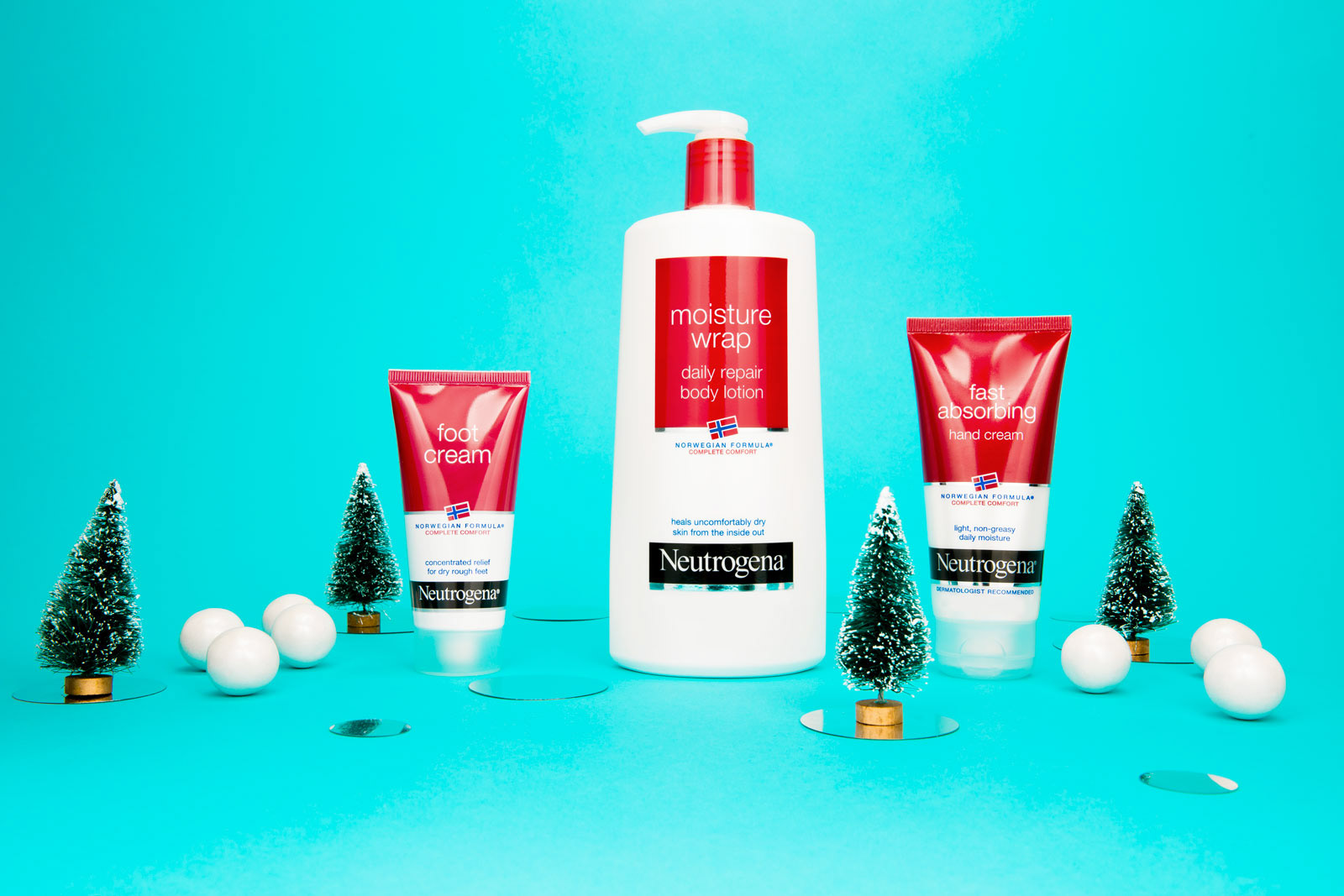 Three lotions are styled against a neon blue background with small bottle brush Christmas tree decorations.
