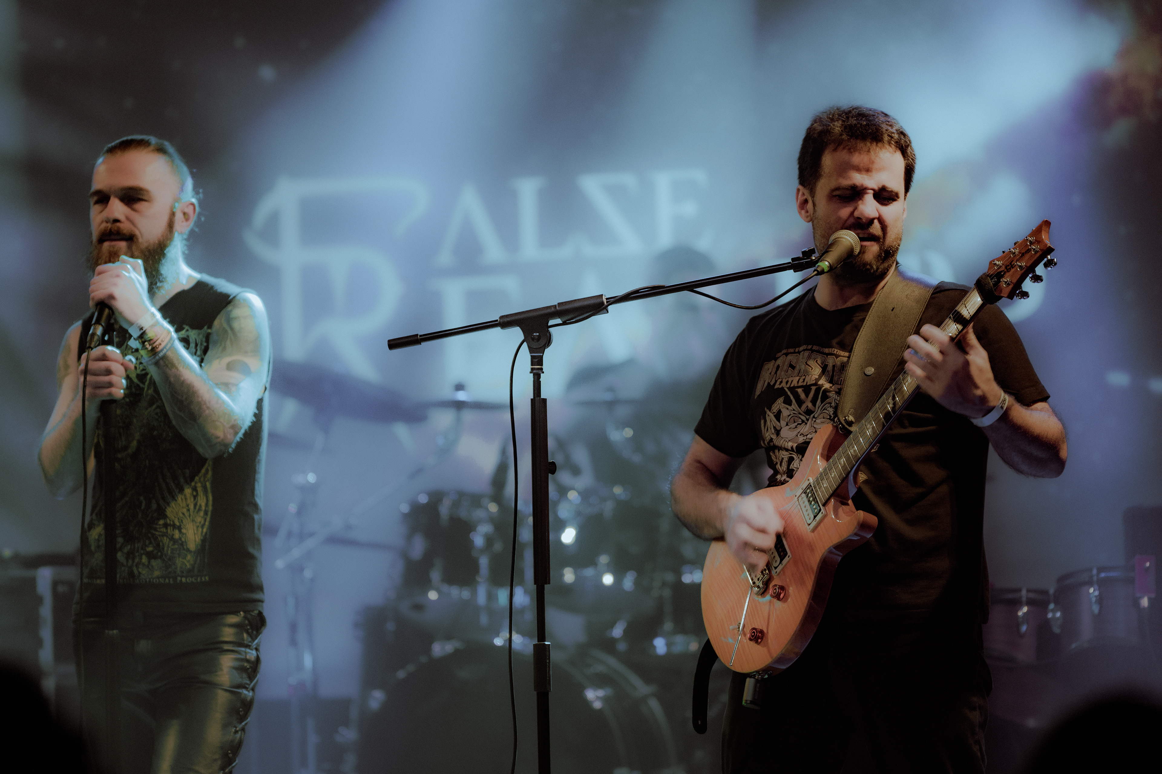 Concert photography of Flase Reality’s guitarist singing alongside the vocalist during a live show at Rockstadt Club in Brașov.