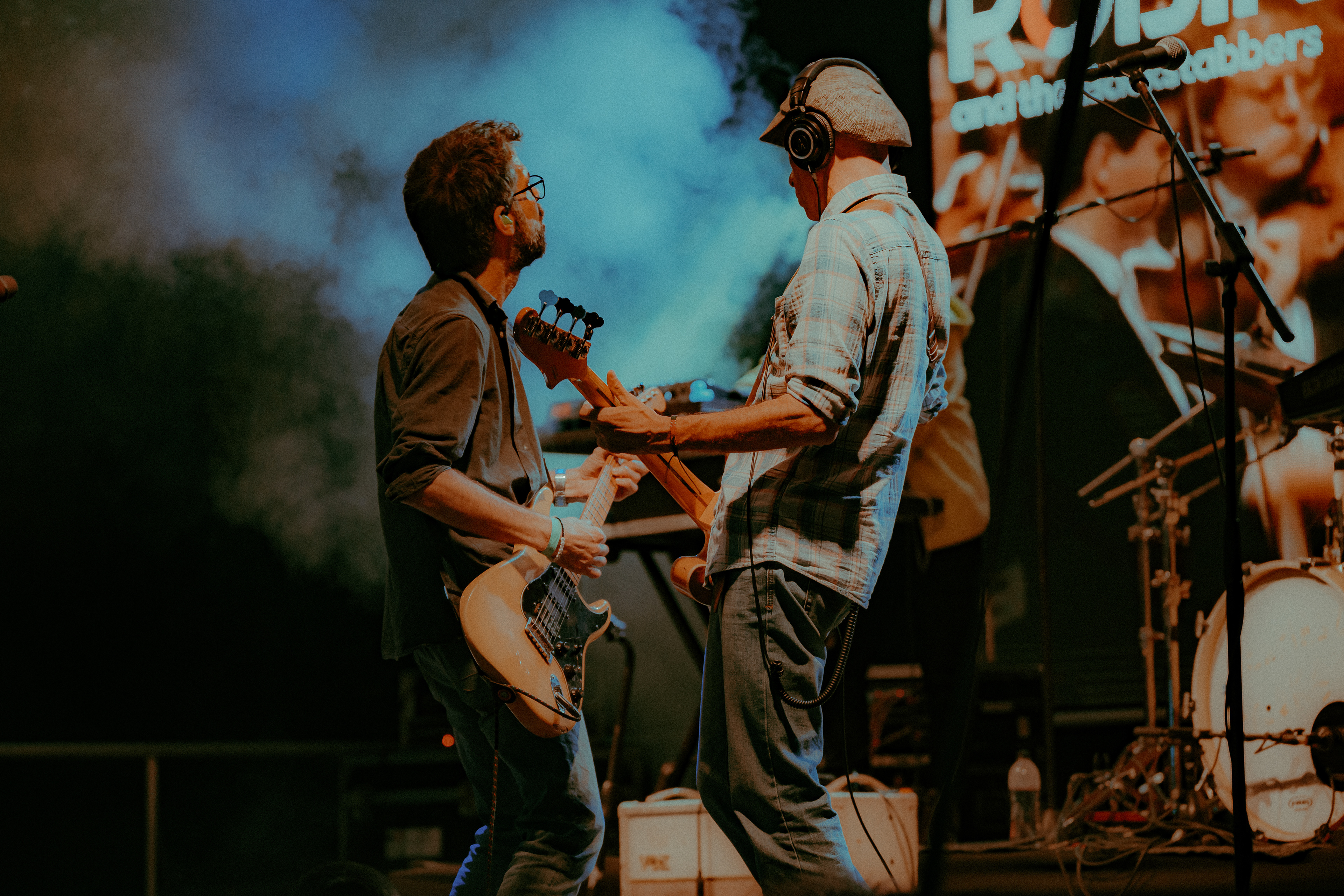 Concert photography showing Robin and the Backstabbers vocalist, guitarist, and bassist dancing and performing closely together on stage.