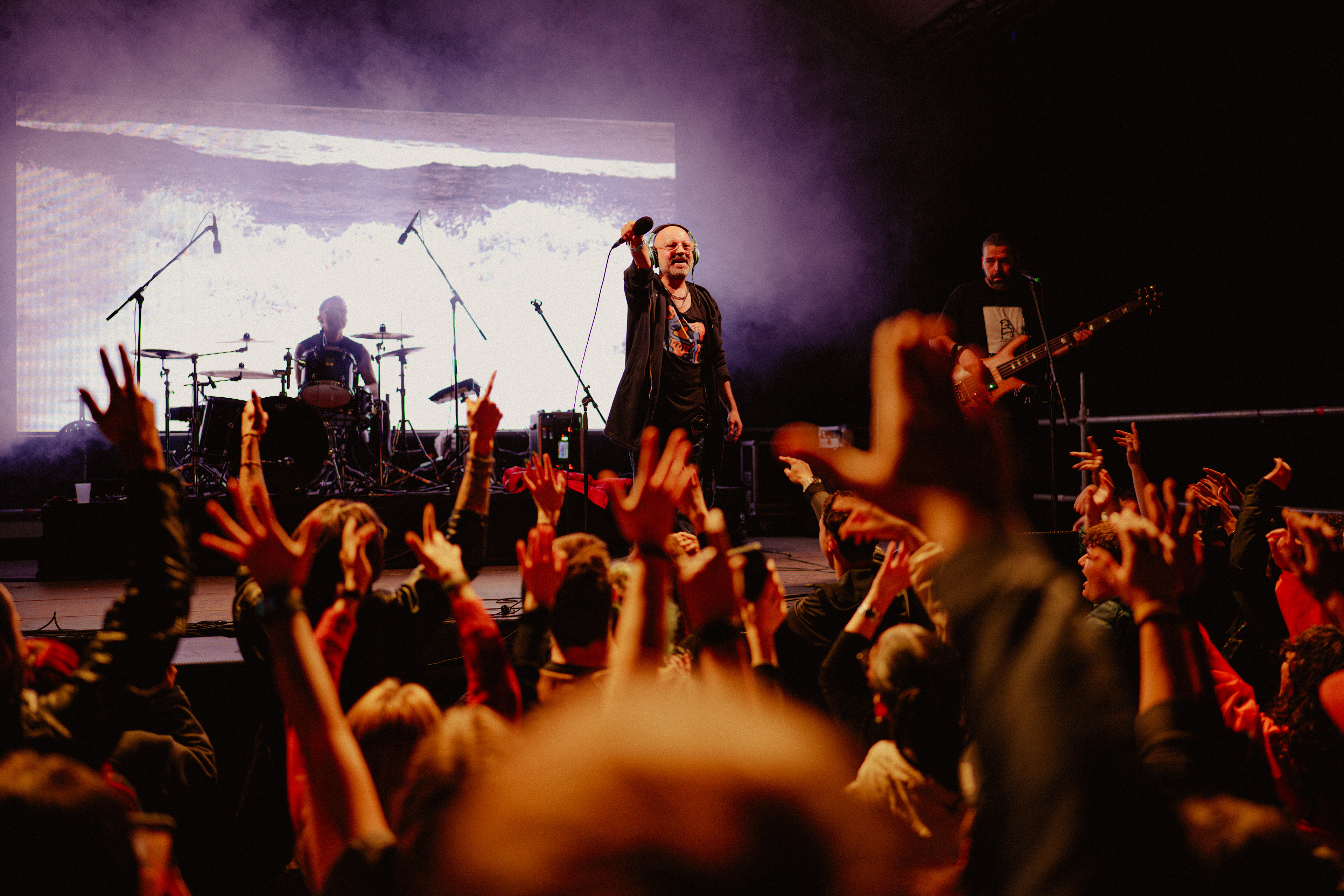 Concert photography of Omul cu Șobolani’s vocalist holding the microphone towards the crowd as fans raise their hands and sing along.