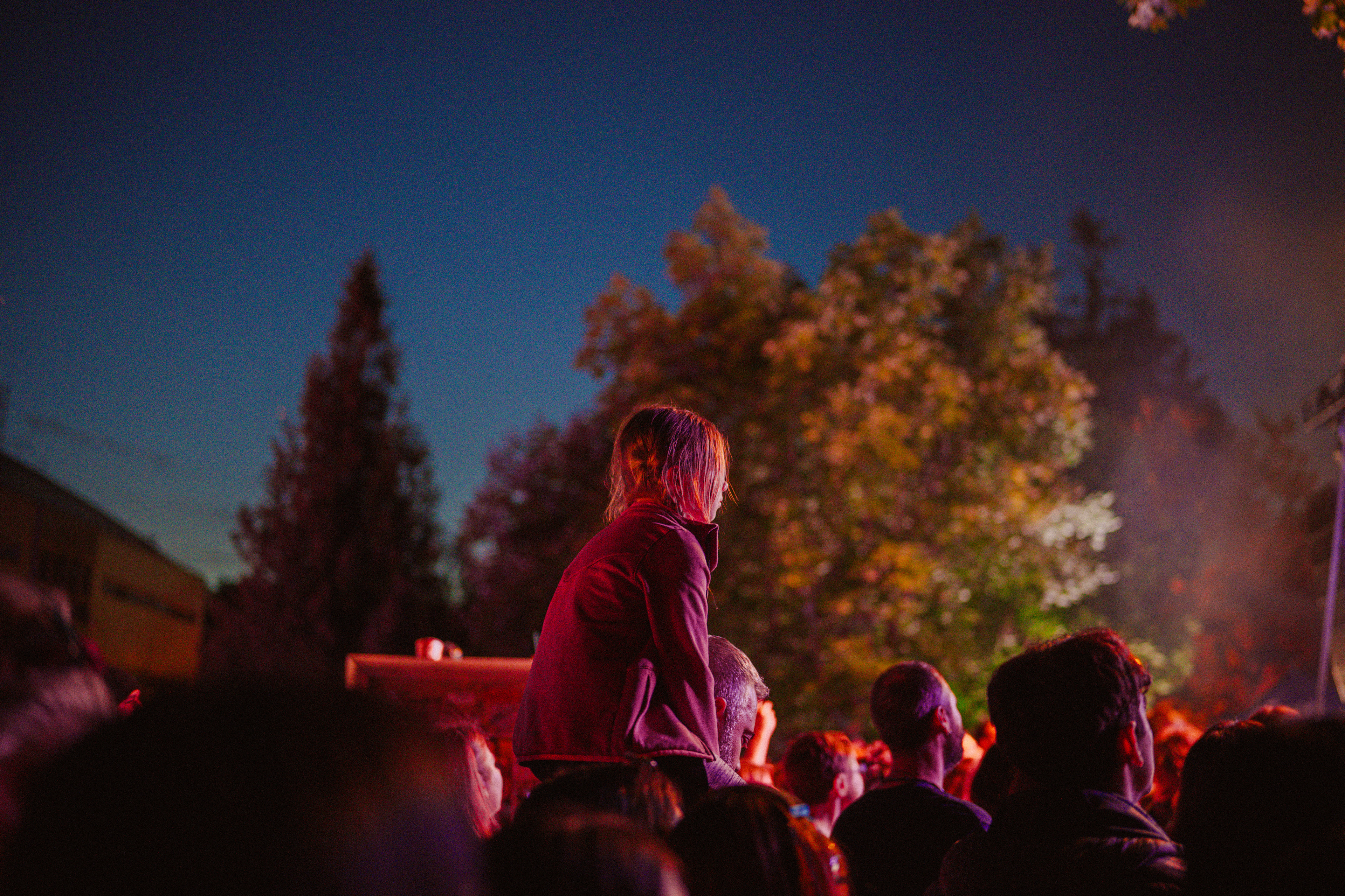 Live event photography capturing a child sitting on her father’s shoulders, watching Om La Luna perform on stage.