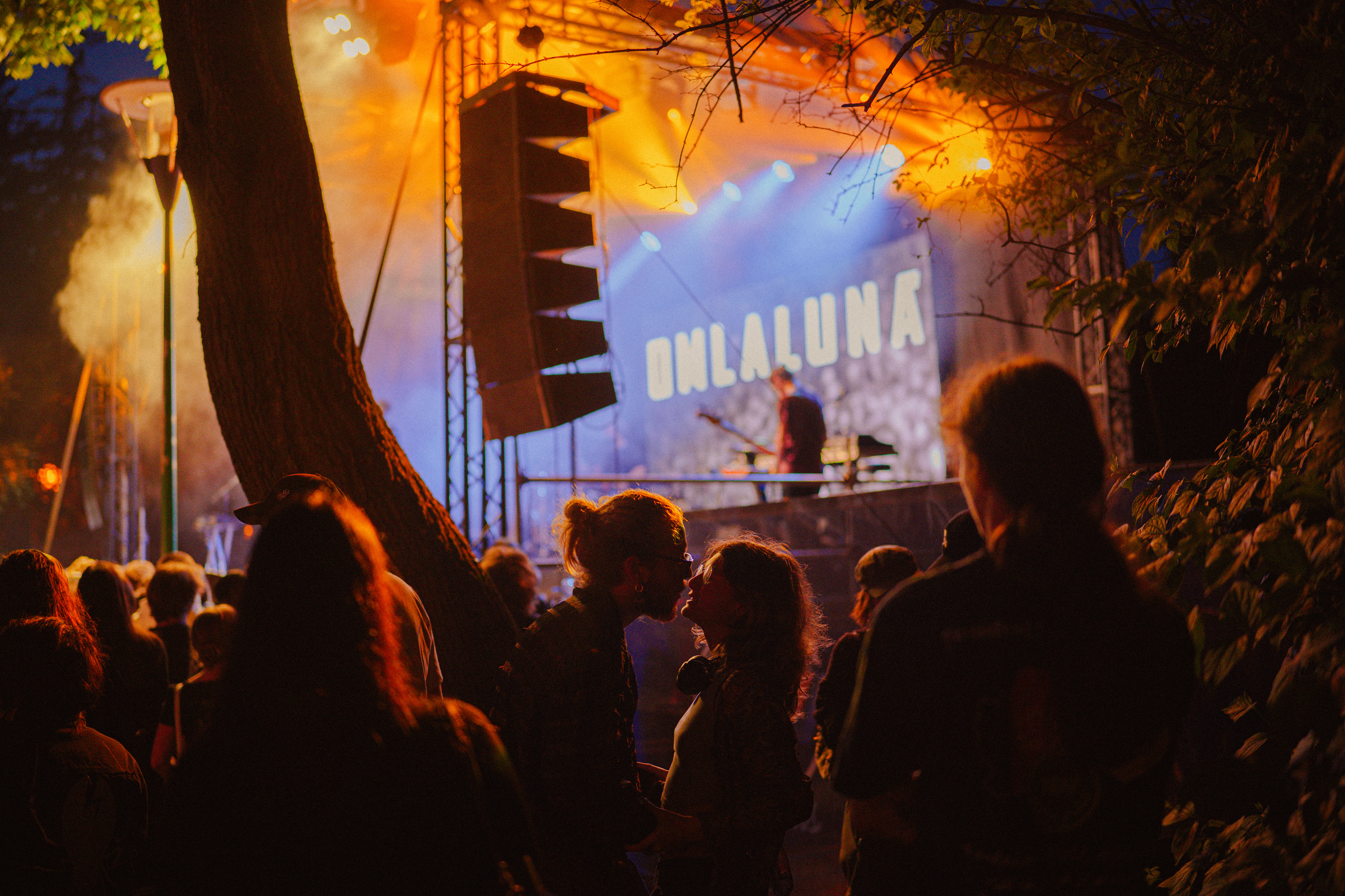 Concert photography capturing a couple kissing tenderly alongside the stage during Om La Luna’s live performance.