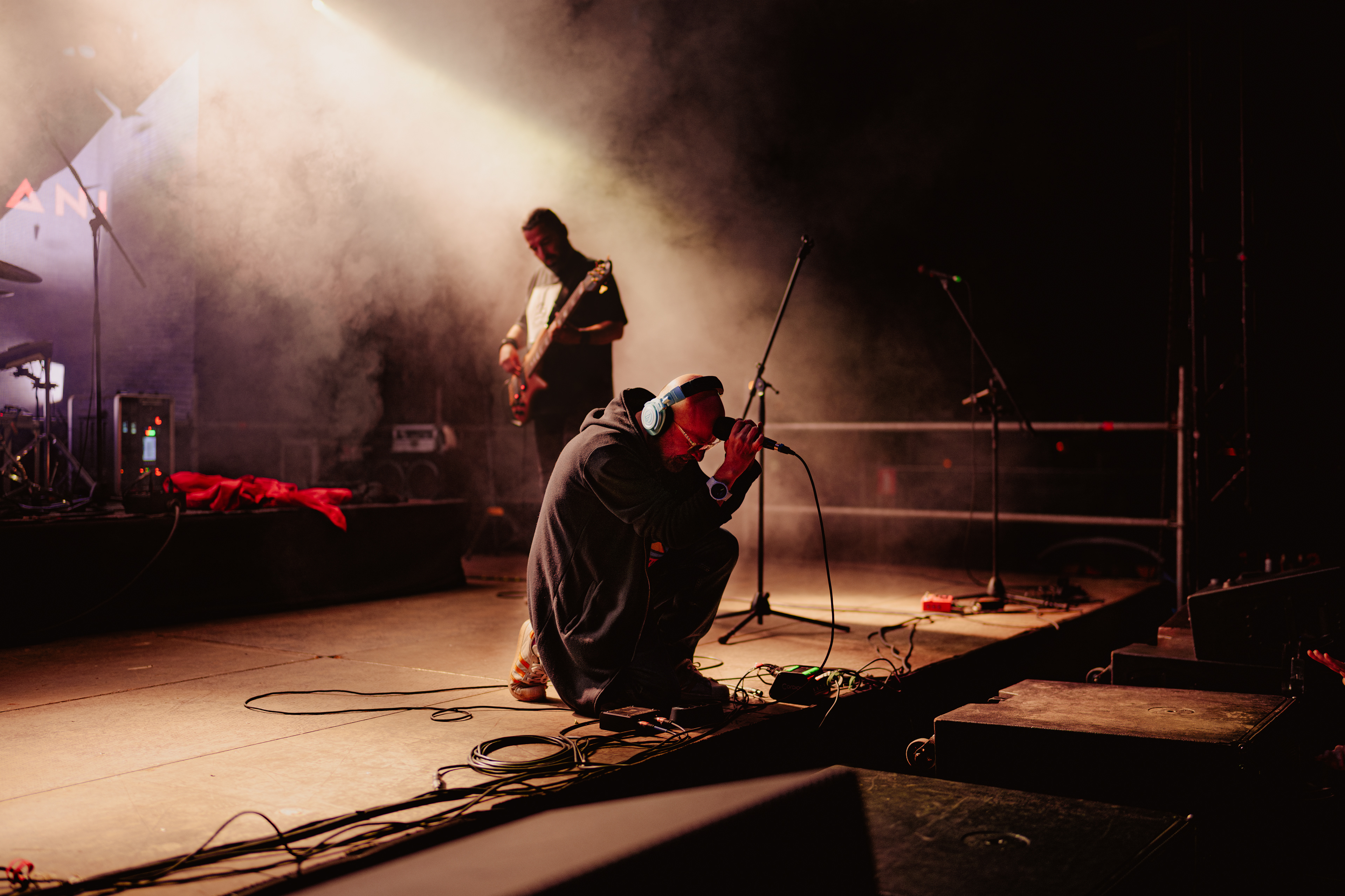 Concert photography of Omul cu Șobolani vocalist sitting on his knees with microphone resting on his head during a powerful live performance.