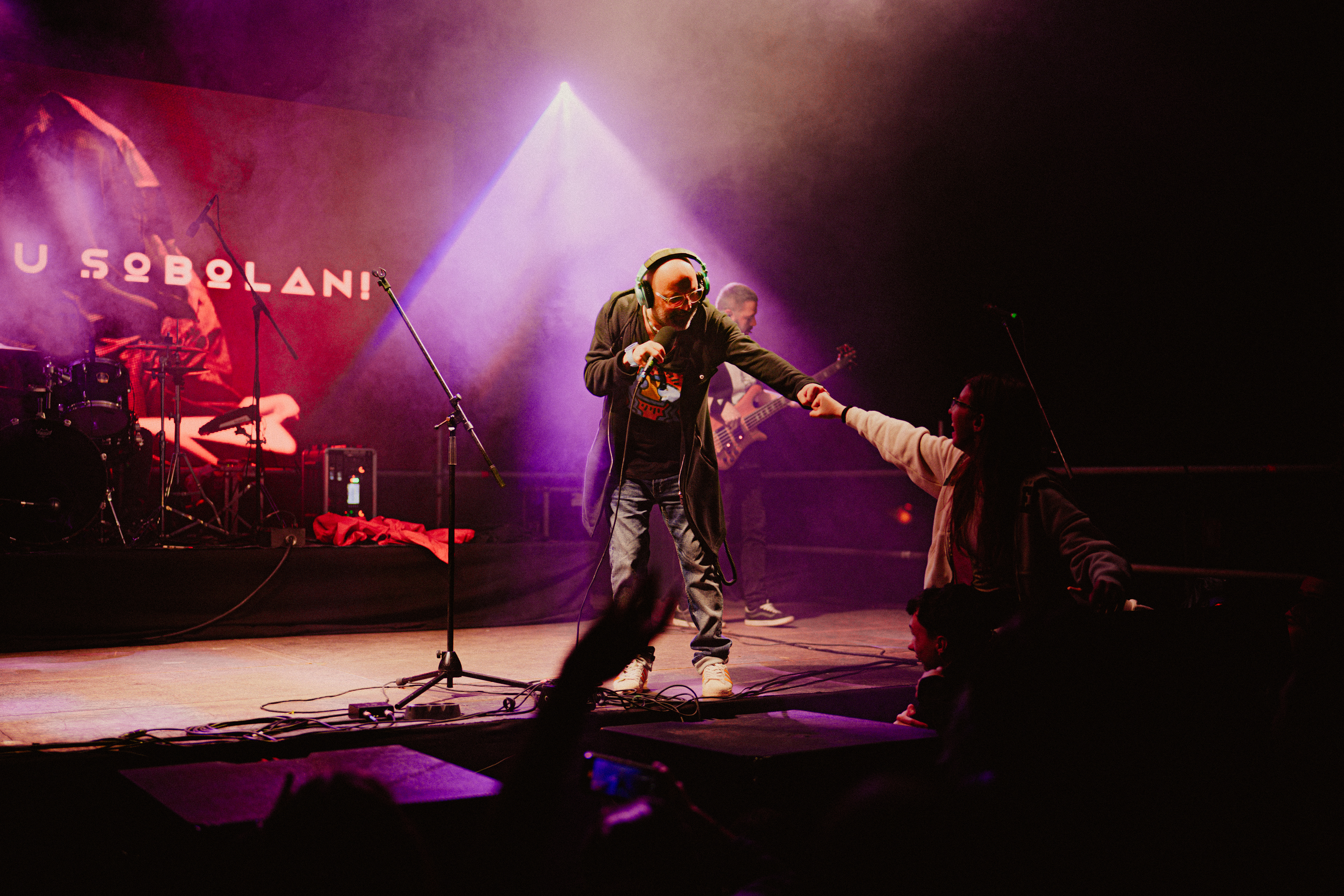 Concert photography of Omul cu Șobolani’s vocalist fist bumping a fan from the crowd, smiling warmly during the live event.