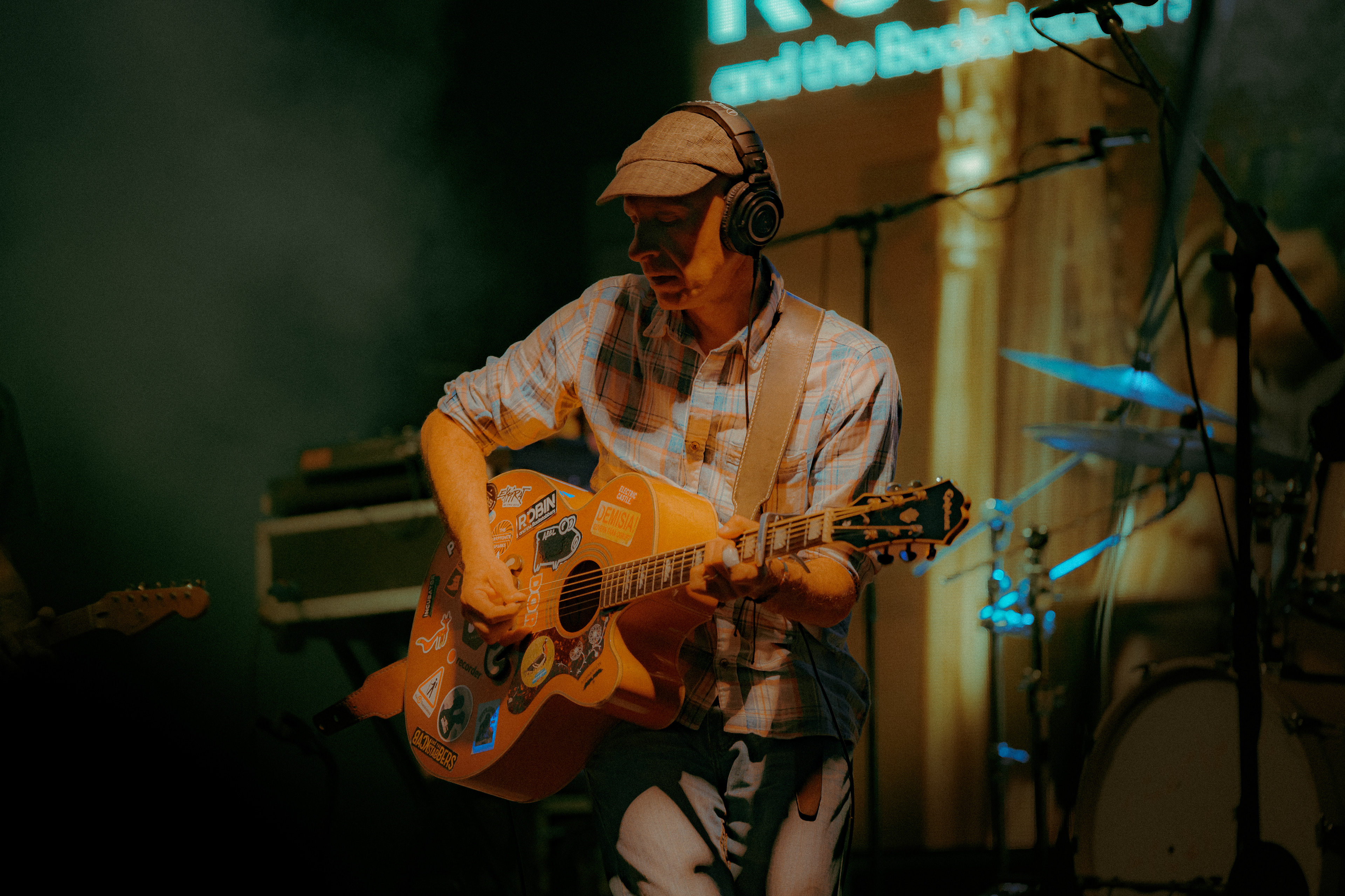 Live performance photo of Robin and the Backstabbers guitarist singing and playing acoustic guitar with heartfelt emotion.