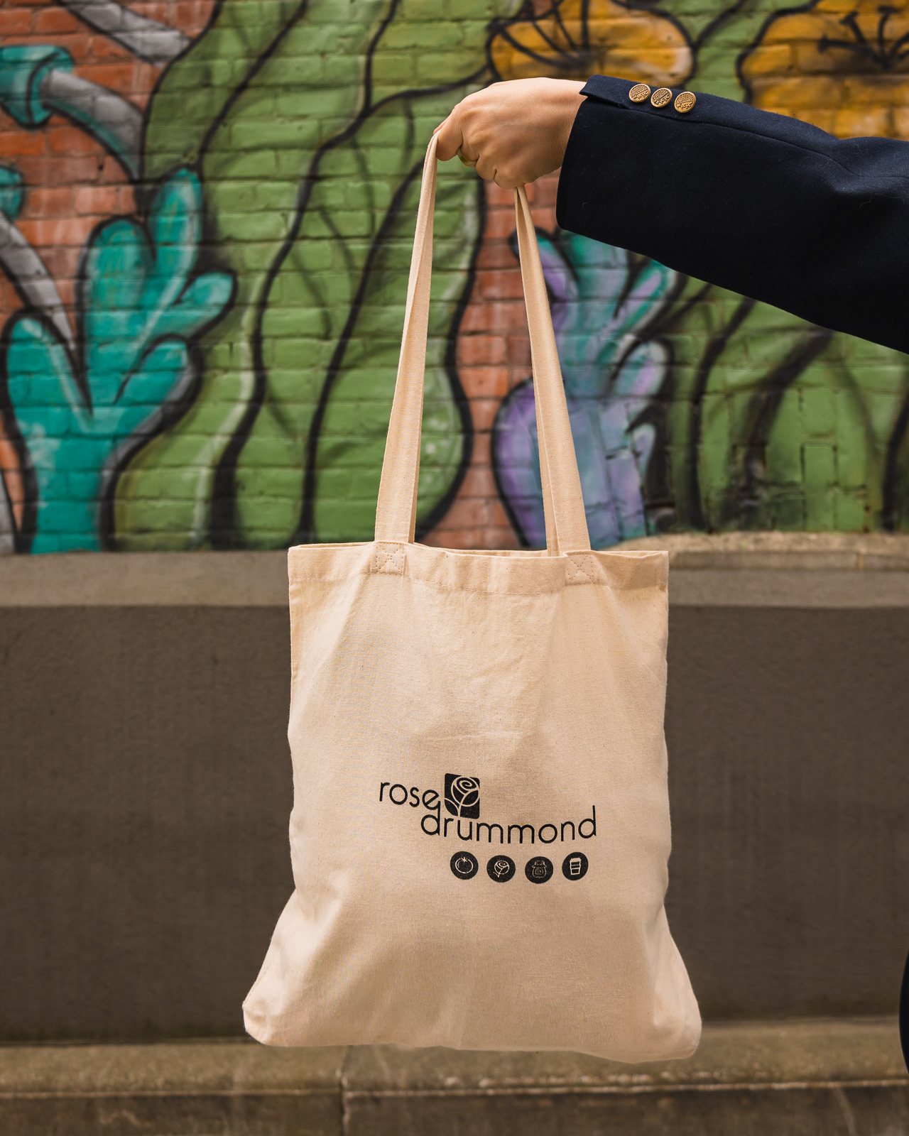 Hand holding a tote bag in front of a colourful wall