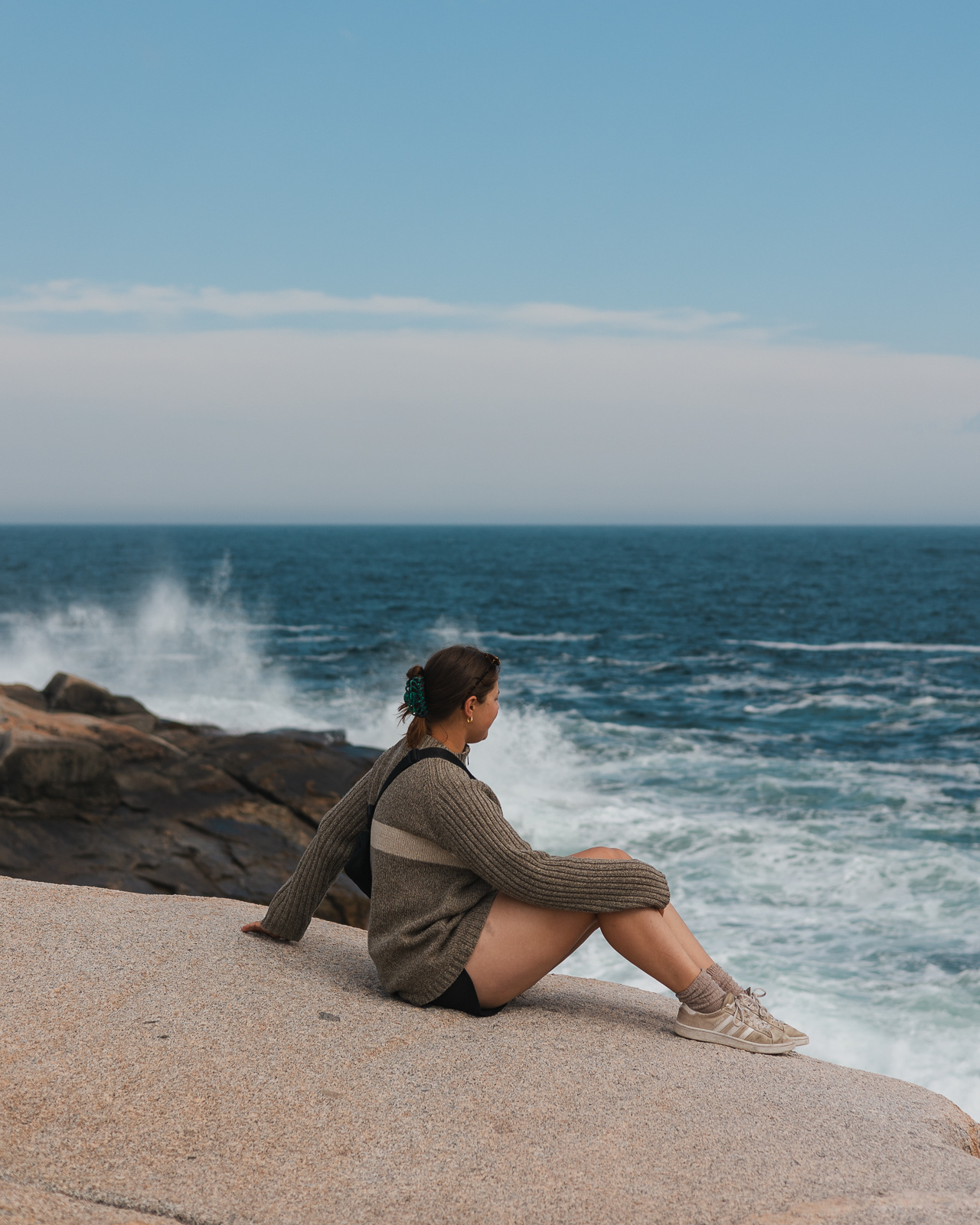Woman sitting on a cliff overlooking the Atlantic ocean in Peggy's Cove, Canada
