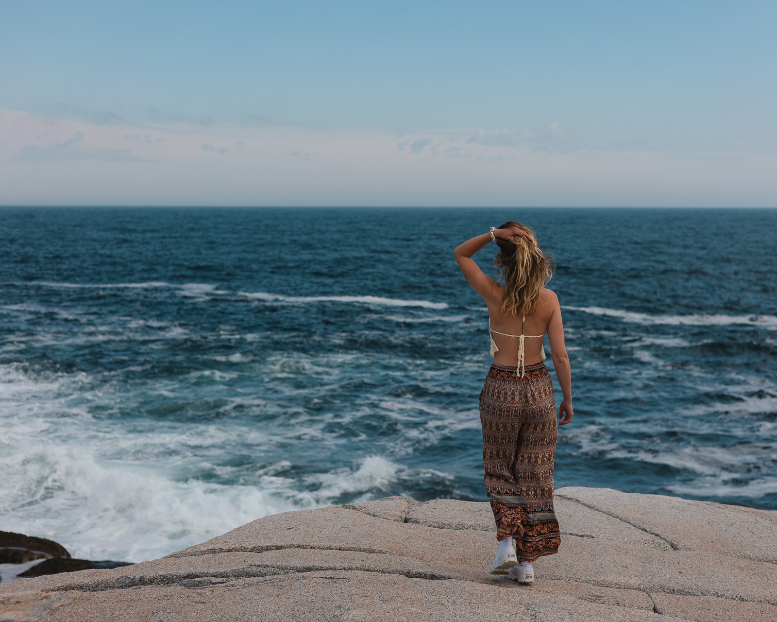Woman walking towards the Atlantic ocean on a cliff in Peggy's Cove, Nova Scotia