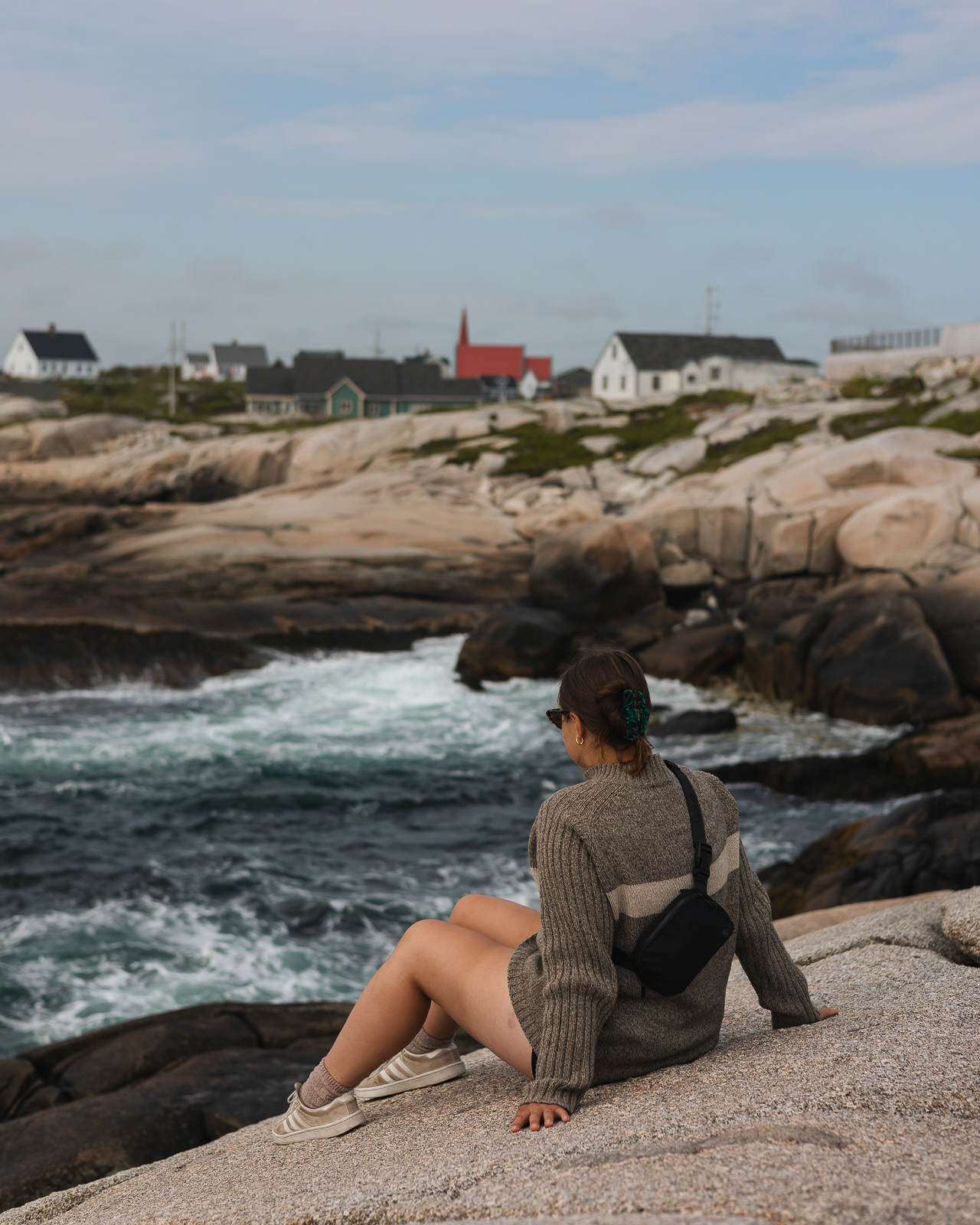 Woman sitting on a cliff overlooking Peggy's Cove town in Nova Scotia, Canada