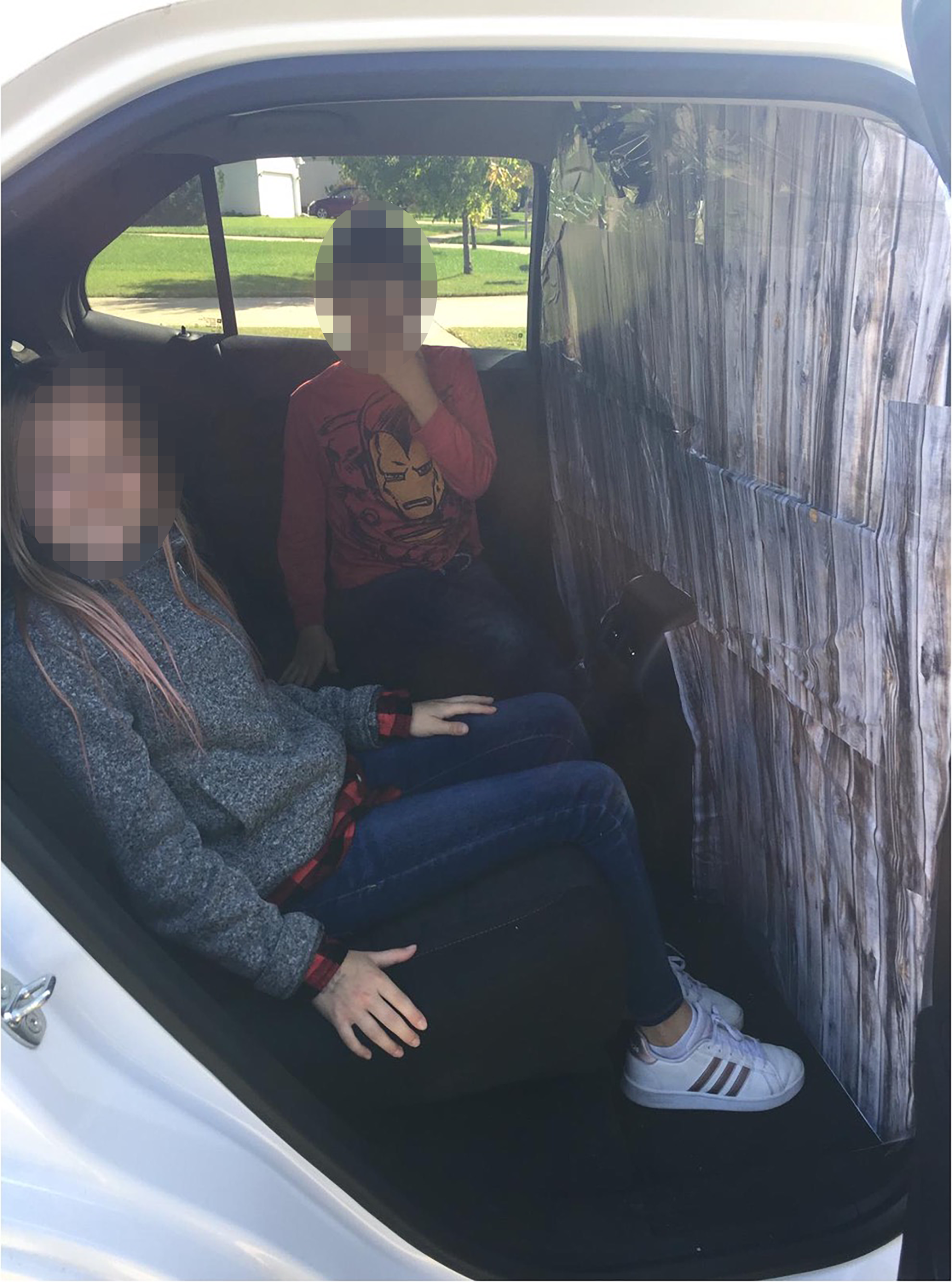 Two children are seated in the back seat of a white SUV. A barrier is installed between the back seats and the driver seat.